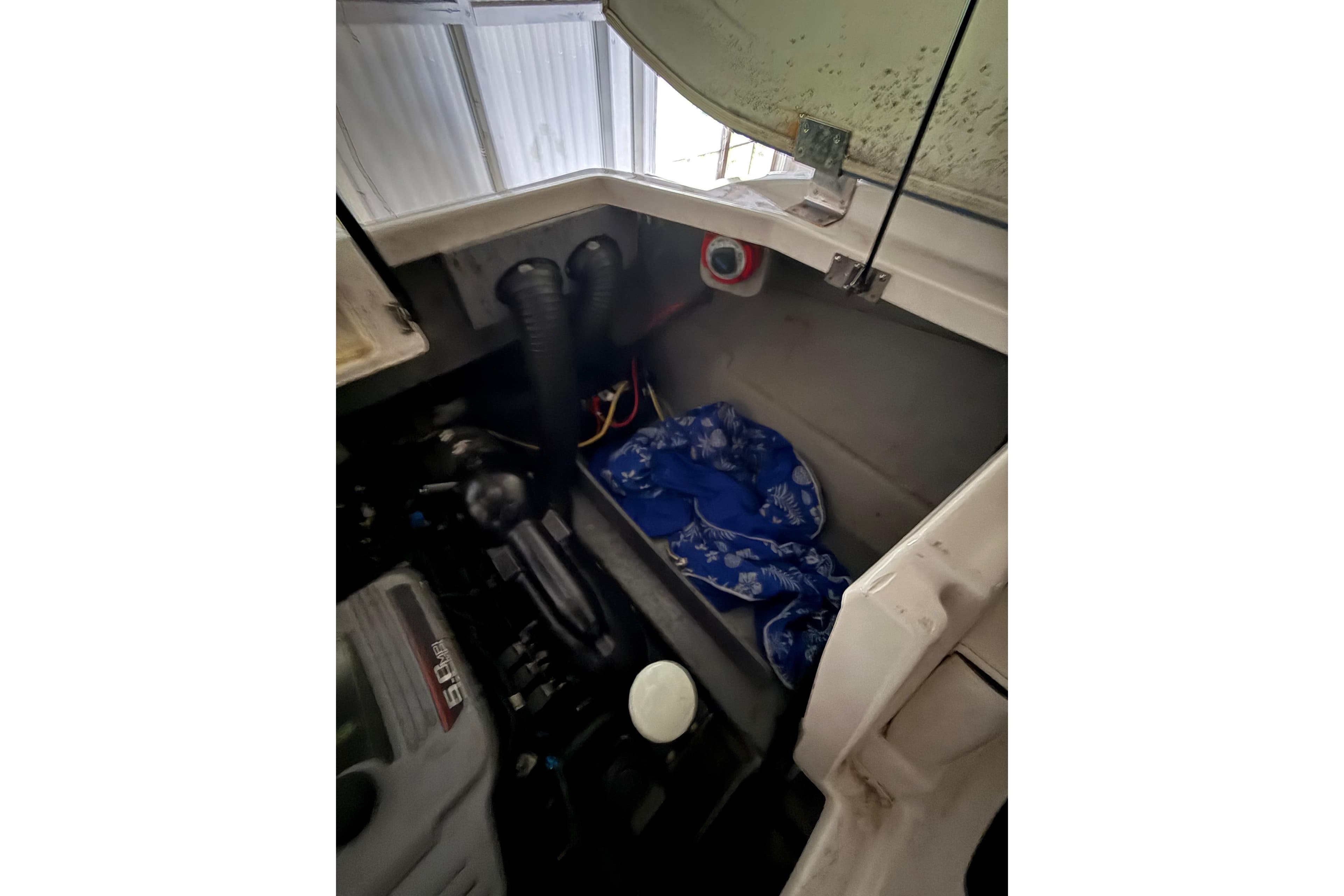 Engine compartment of a 2012 Bayliner 235 Bowrider with visible components and storage area.