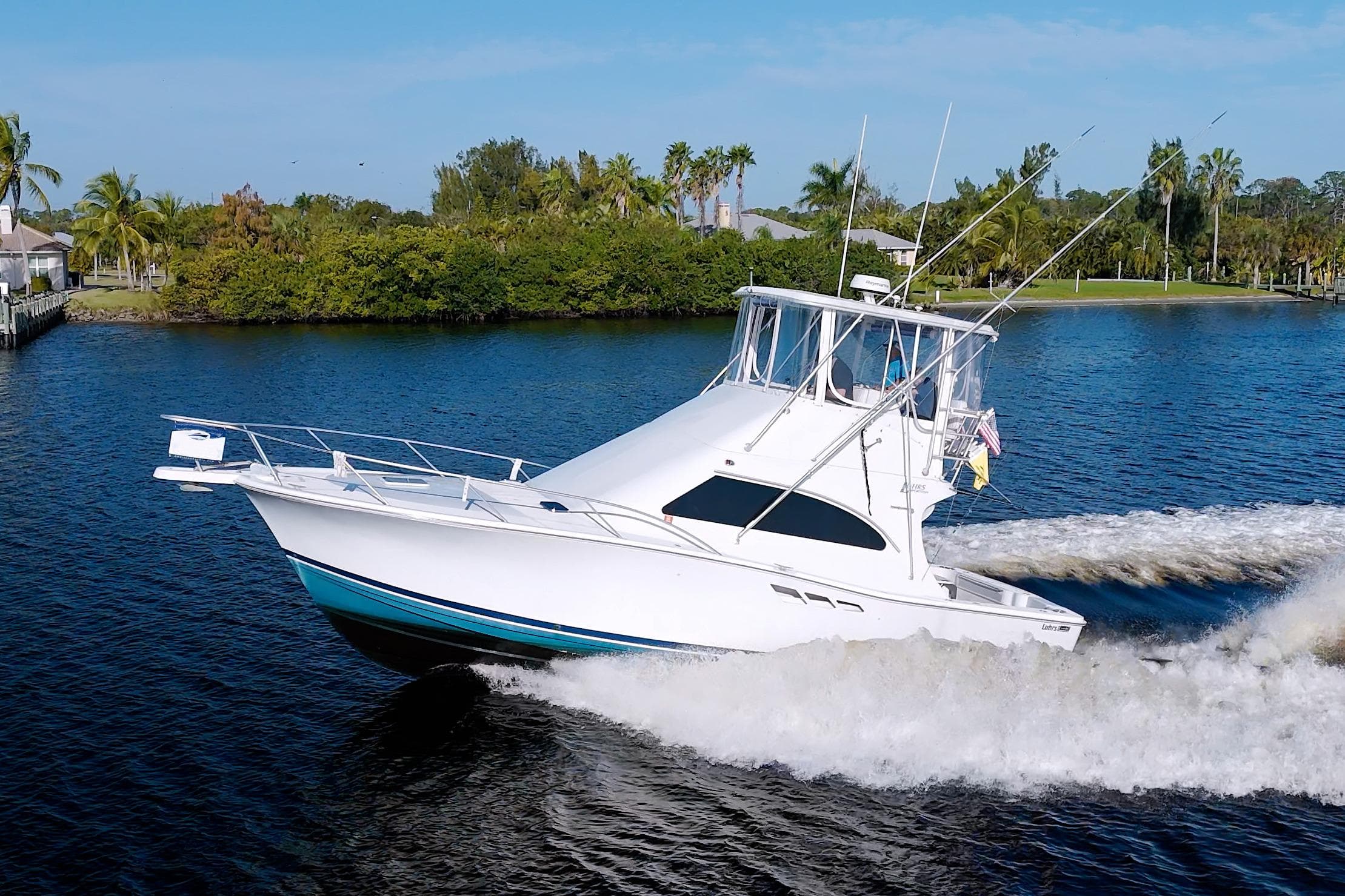 1998 Luhrs 36 Convertible yacht cruising on a scenic waterway with lush greenery.