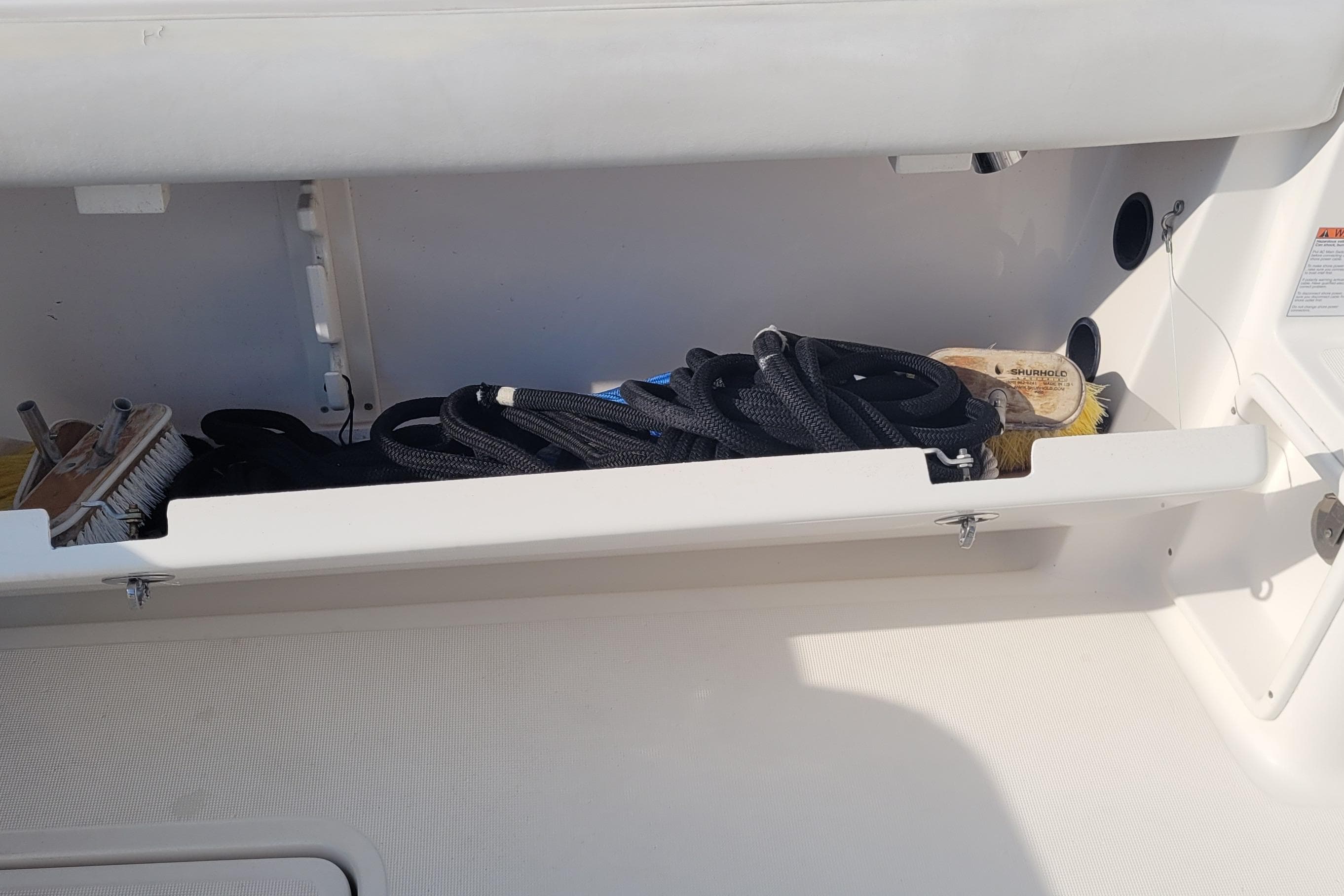 Storage compartment on a 2006 Tiara Yachts 4200 Open, containing ropes and cleaning brushes.