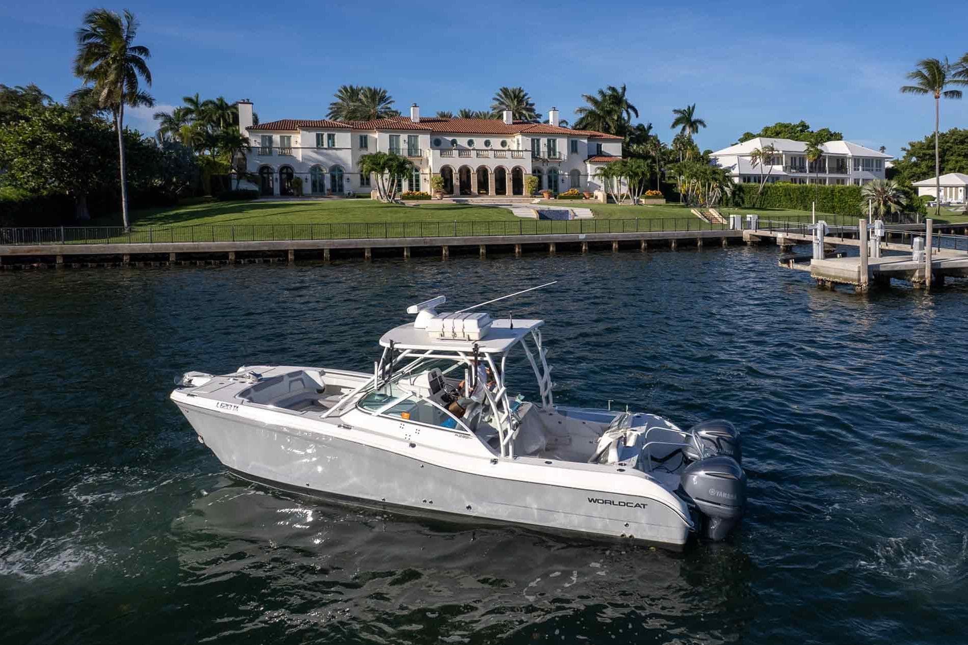 2017 World Cat 295 DC boat cruising near a luxurious waterfront mansion.