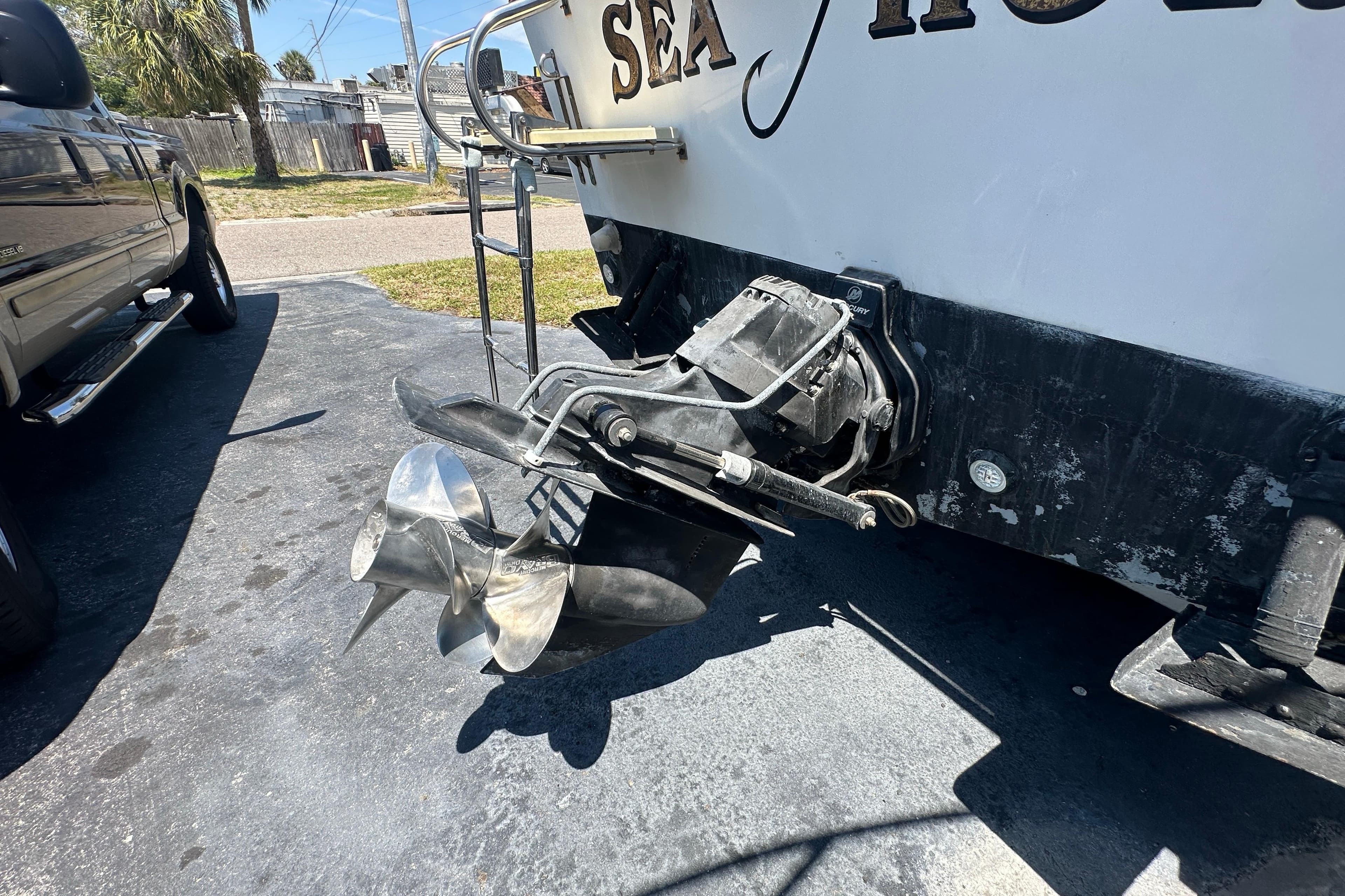 1998 True World Marine TE286 boat with dual propellers and ladder, parked on pavement.