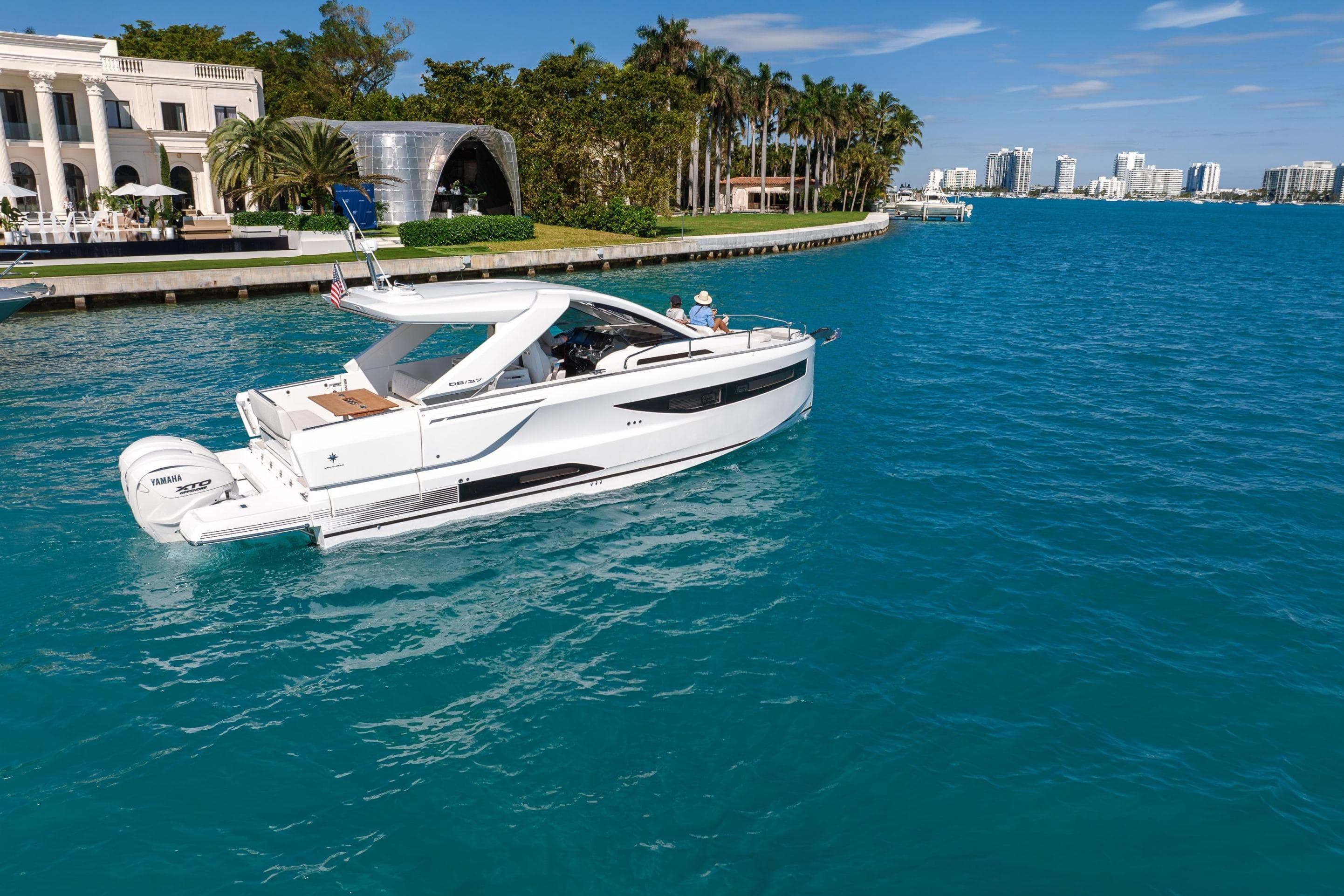 2026 Jeanneau DB/37 OB yacht cruising in clear blue waters near luxury waterfront homes.