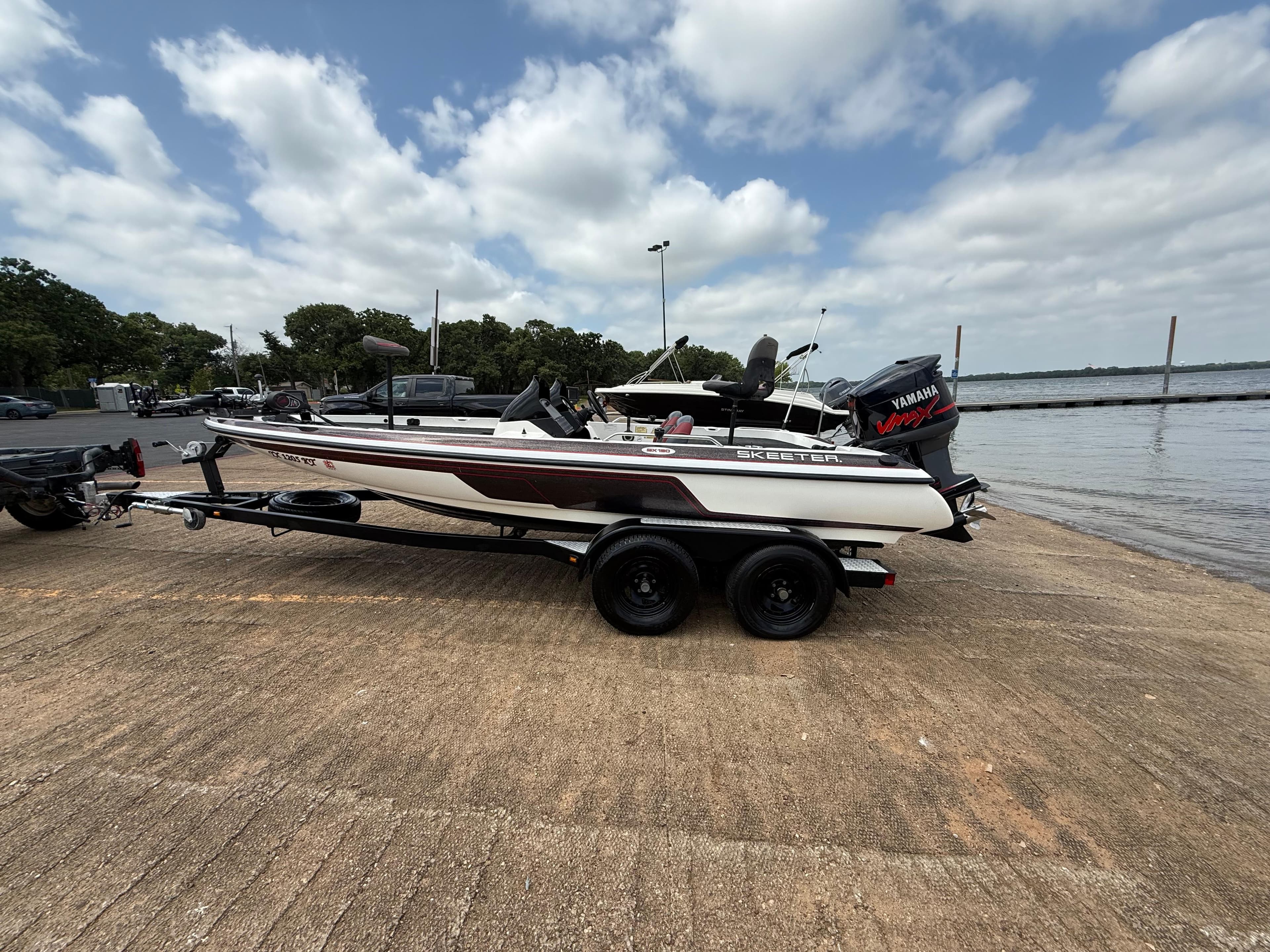 2003 Skeeter SX190 boat on trailer by lakeside under cloudy sky.