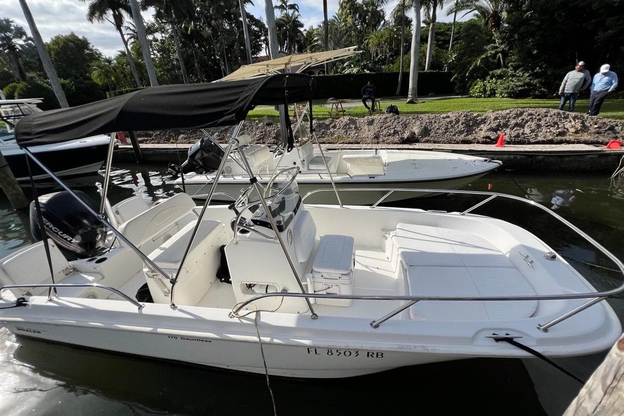 2016 Boston Whaler 170 Dauntless boat docked, featuring a black canopy and white seating.
