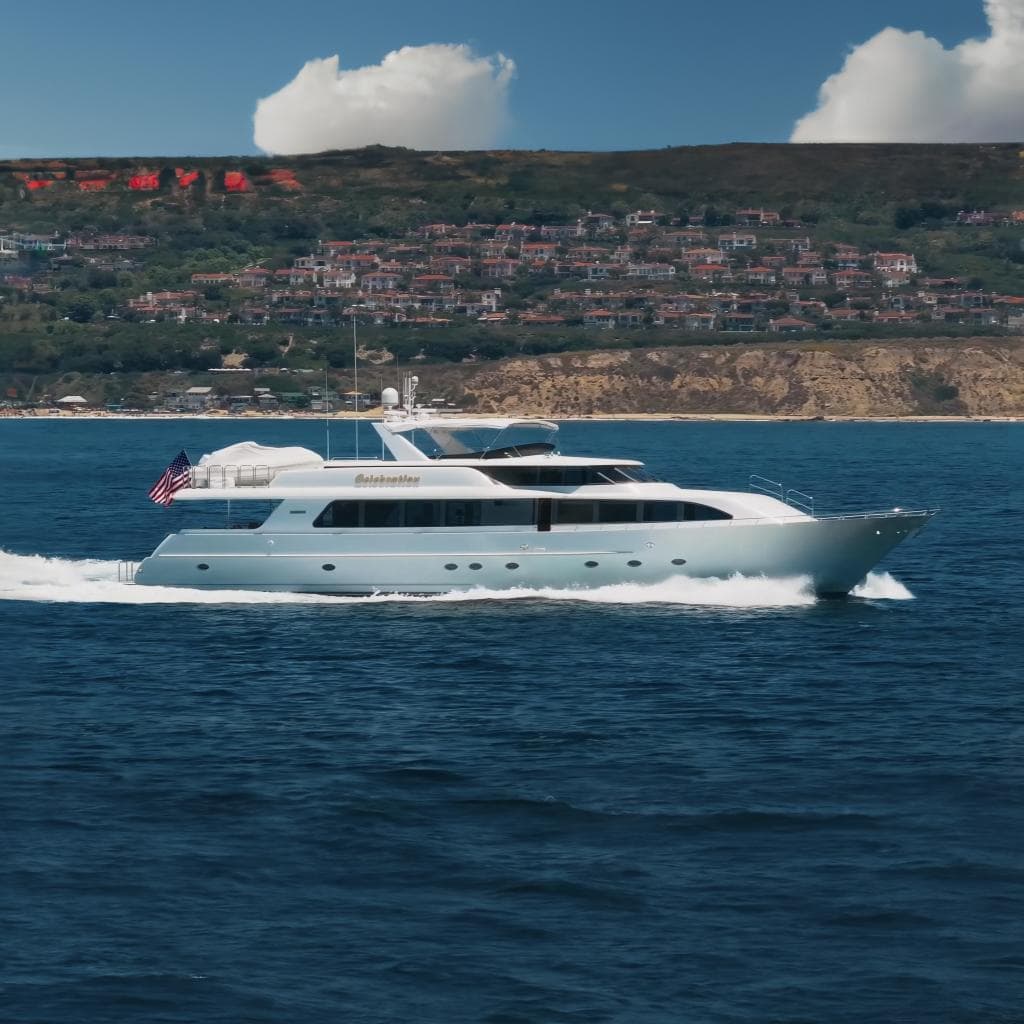 Luxurious 2000 Westport 112 yacht cruising near scenic coastline with hillside homes.
