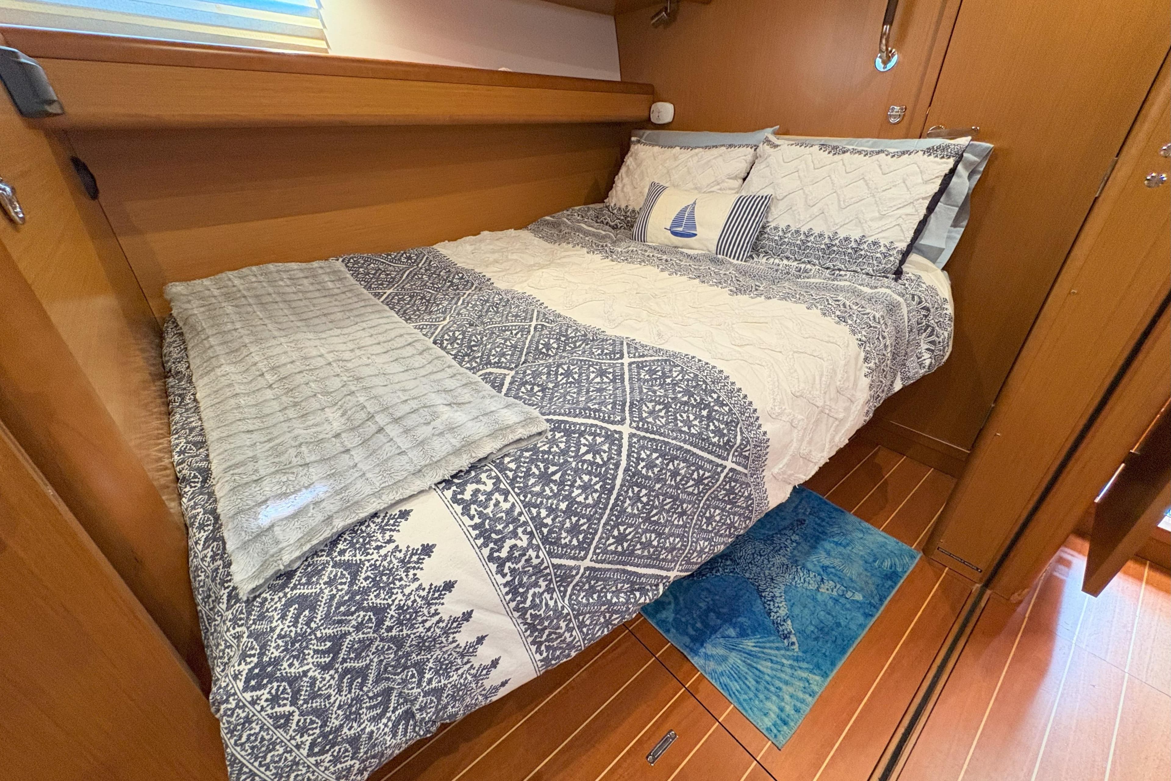 Cozy cabin bedroom in a 2012 Jeanneau 57 yacht with nautical-themed bedding.