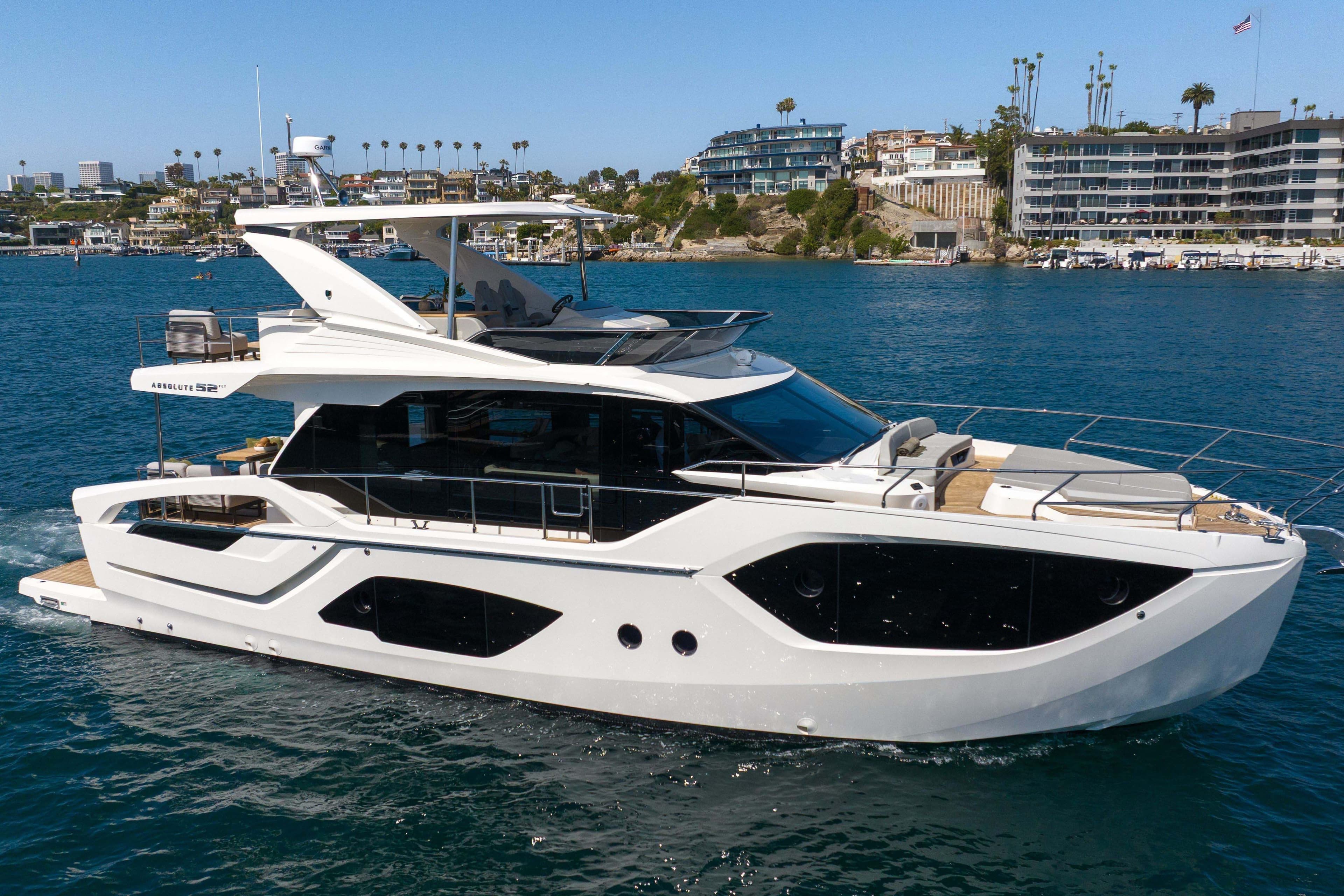 Luxurious 2026 Absolute 52 Fly yacht cruising near a scenic coastal cityscape.