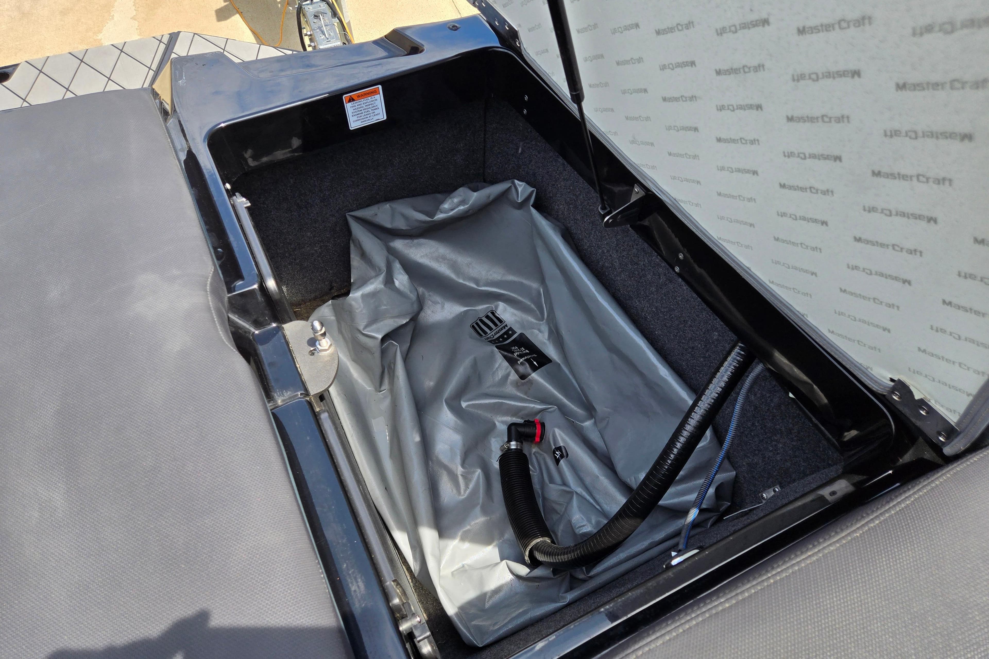 Open storage compartment in 2019 MasterCraft XT25 boat with ballast bag and hose.