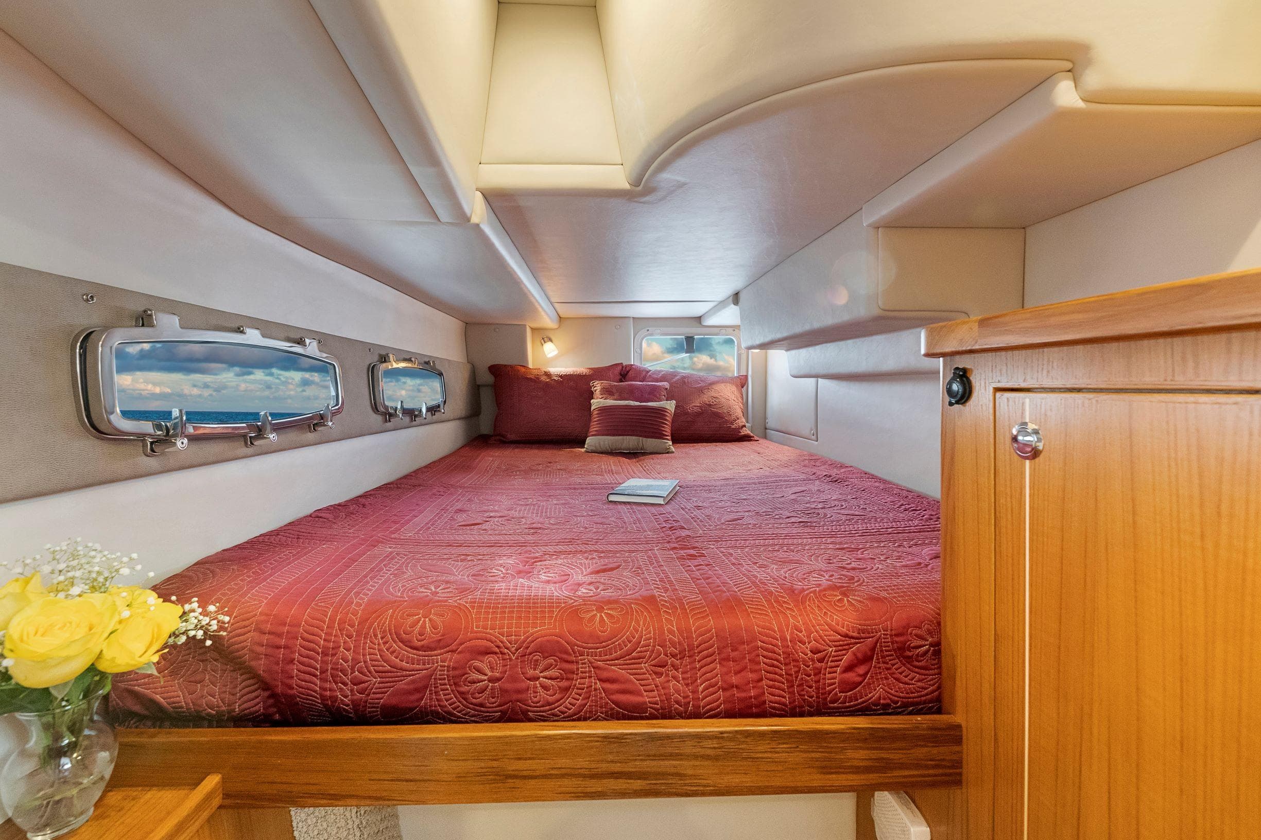 Cozy cabin interior of 2026 Aspen C120 Flybridge with red bedding and wooden accents.