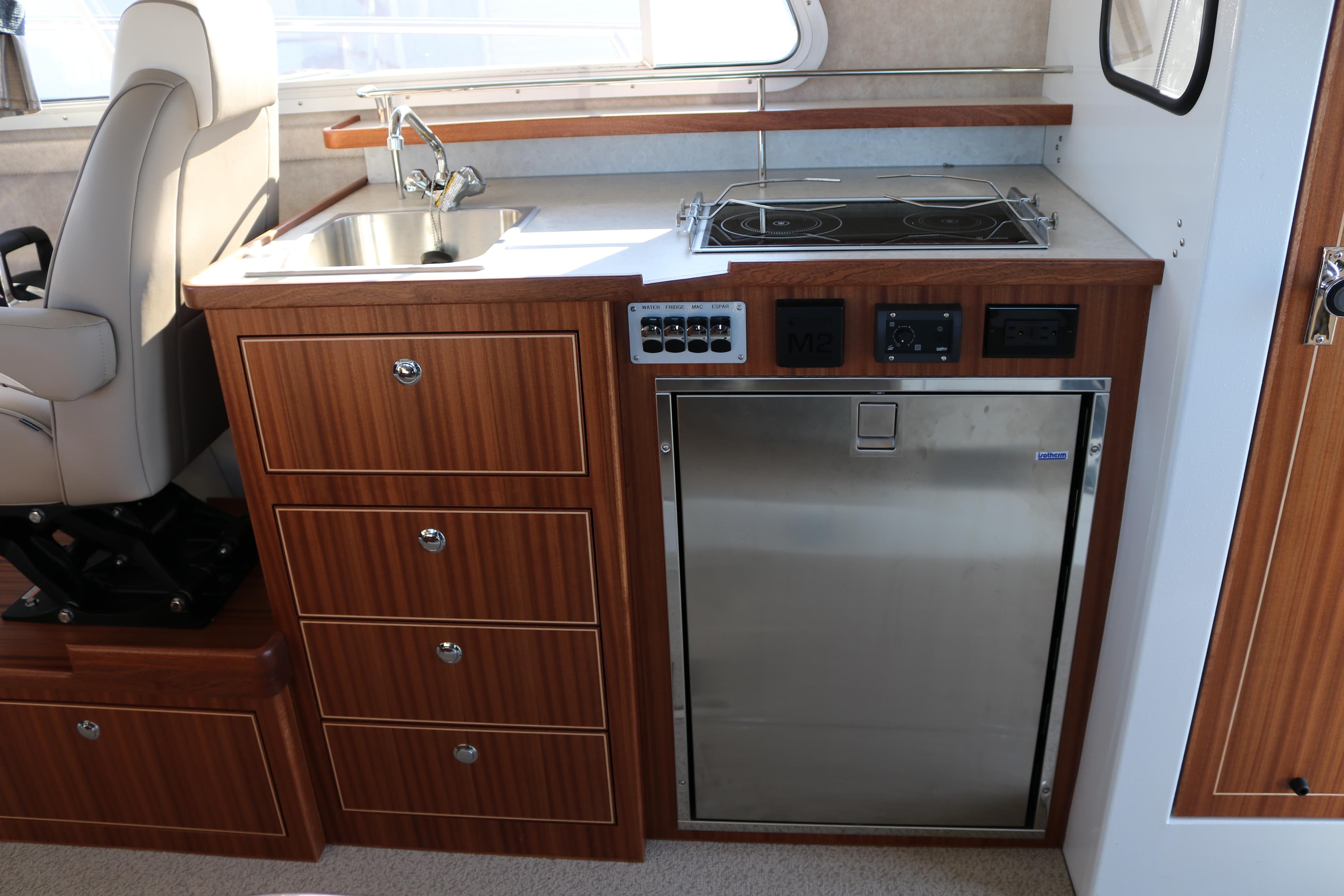 Compact kitchen area in 2026 KingFisher 3425 GFX Offshore boat with sink, stove, and fridge.