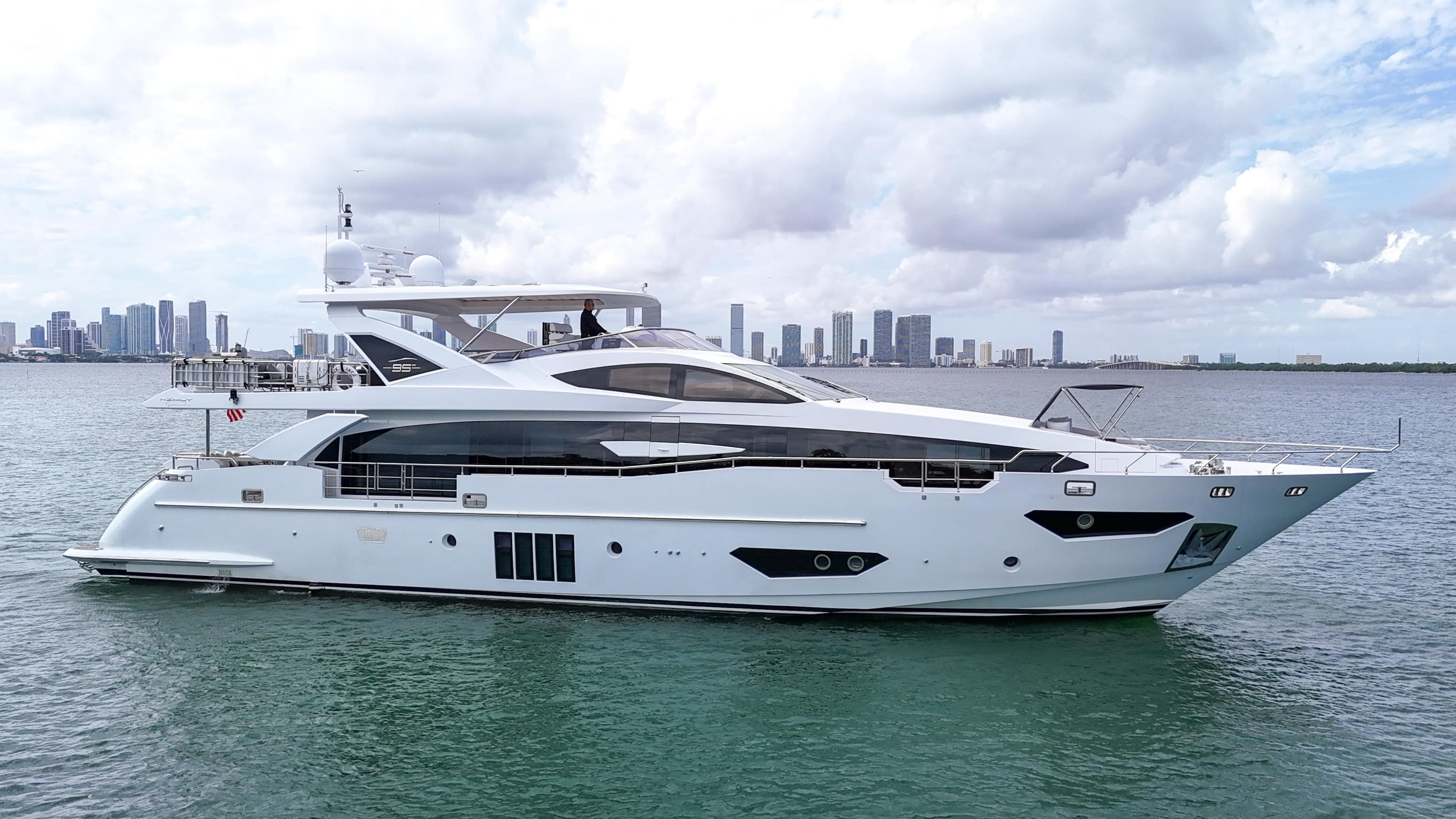 Luxurious 2017 Azimut 95 Raised Pilothouse yacht on calm waters with city skyline backdrop.