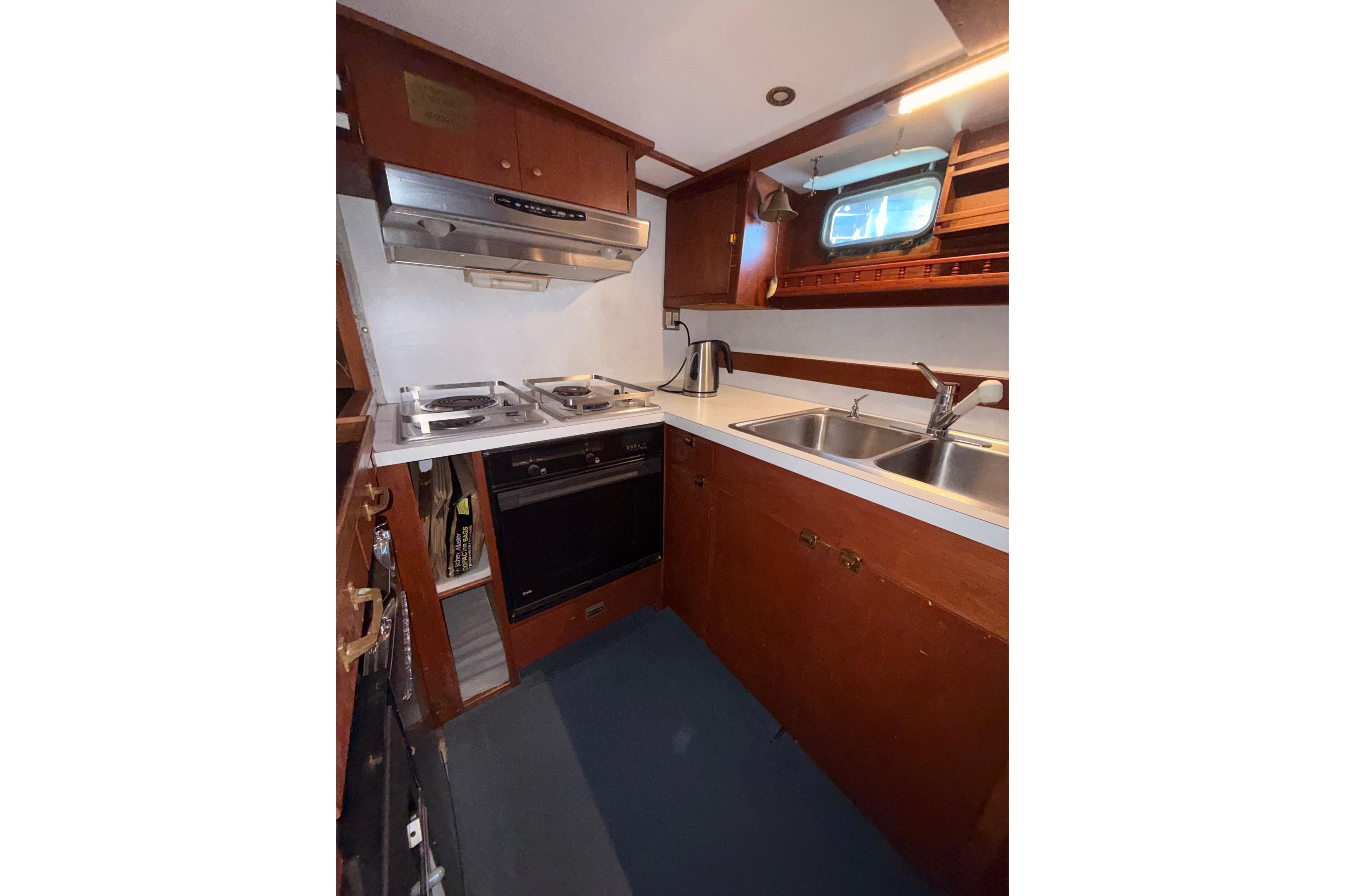1965 Custom Trawler kitchen with stove, oven, dual sink, and wooden cabinetry.