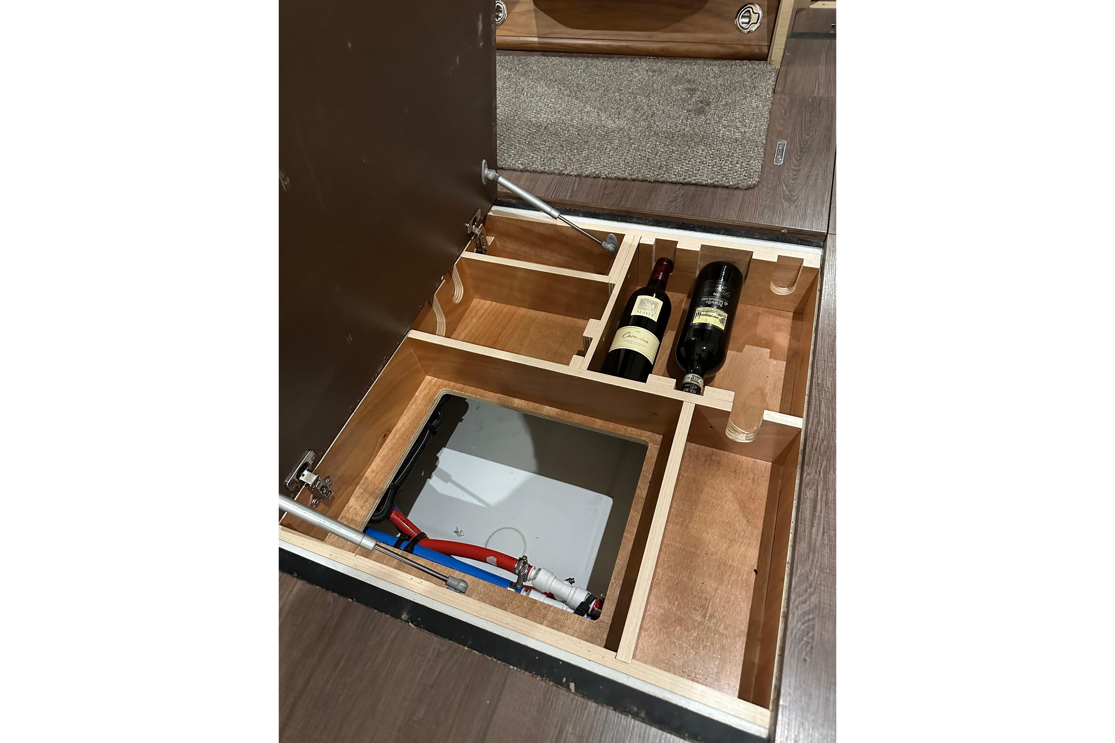 Hidden storage compartment in 2019 Jeanneau 51 yacht with wine bottles and utility access.