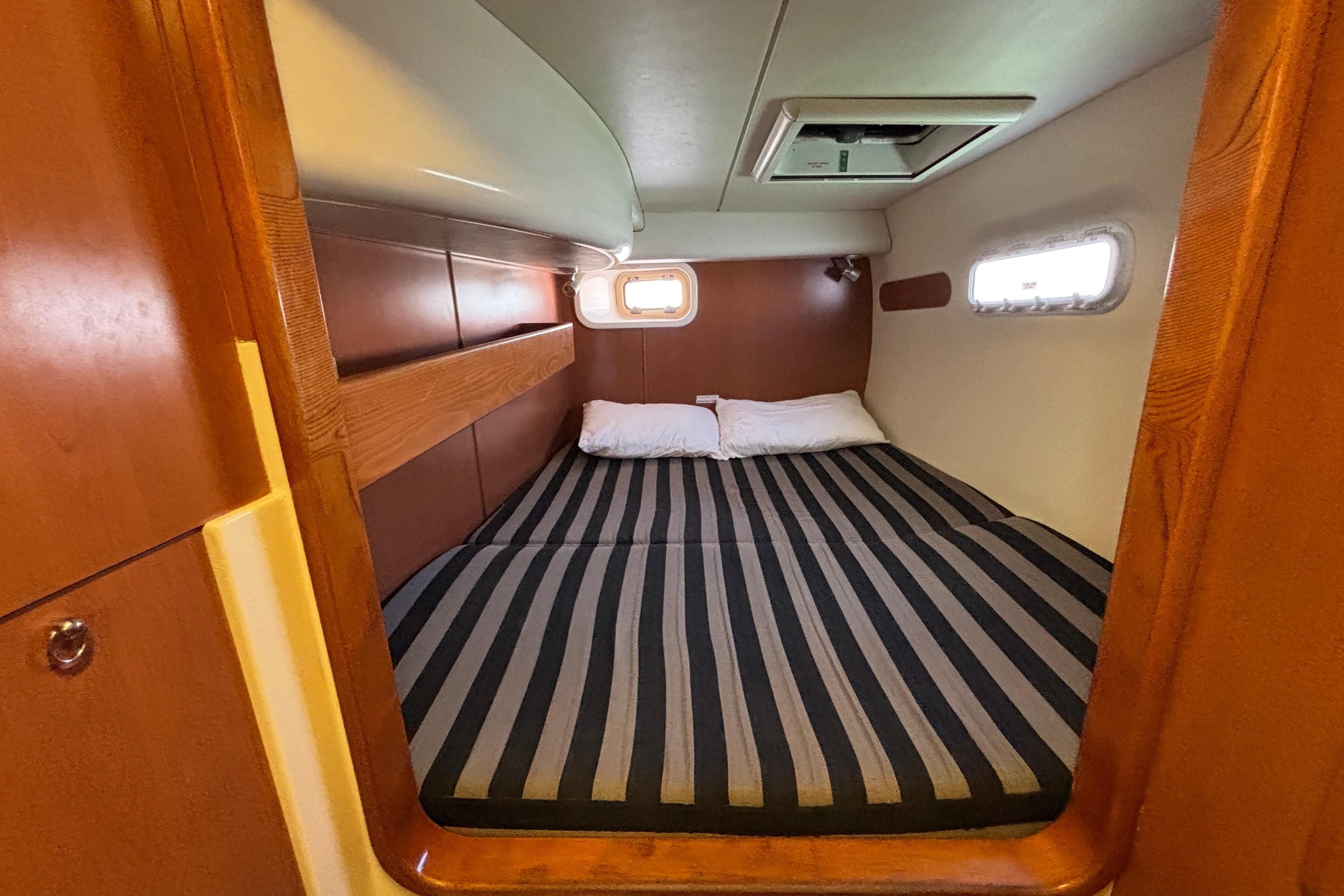 Cozy cabin interior of 2007 Leopard 40 catamaran with striped bedding and wooden accents.