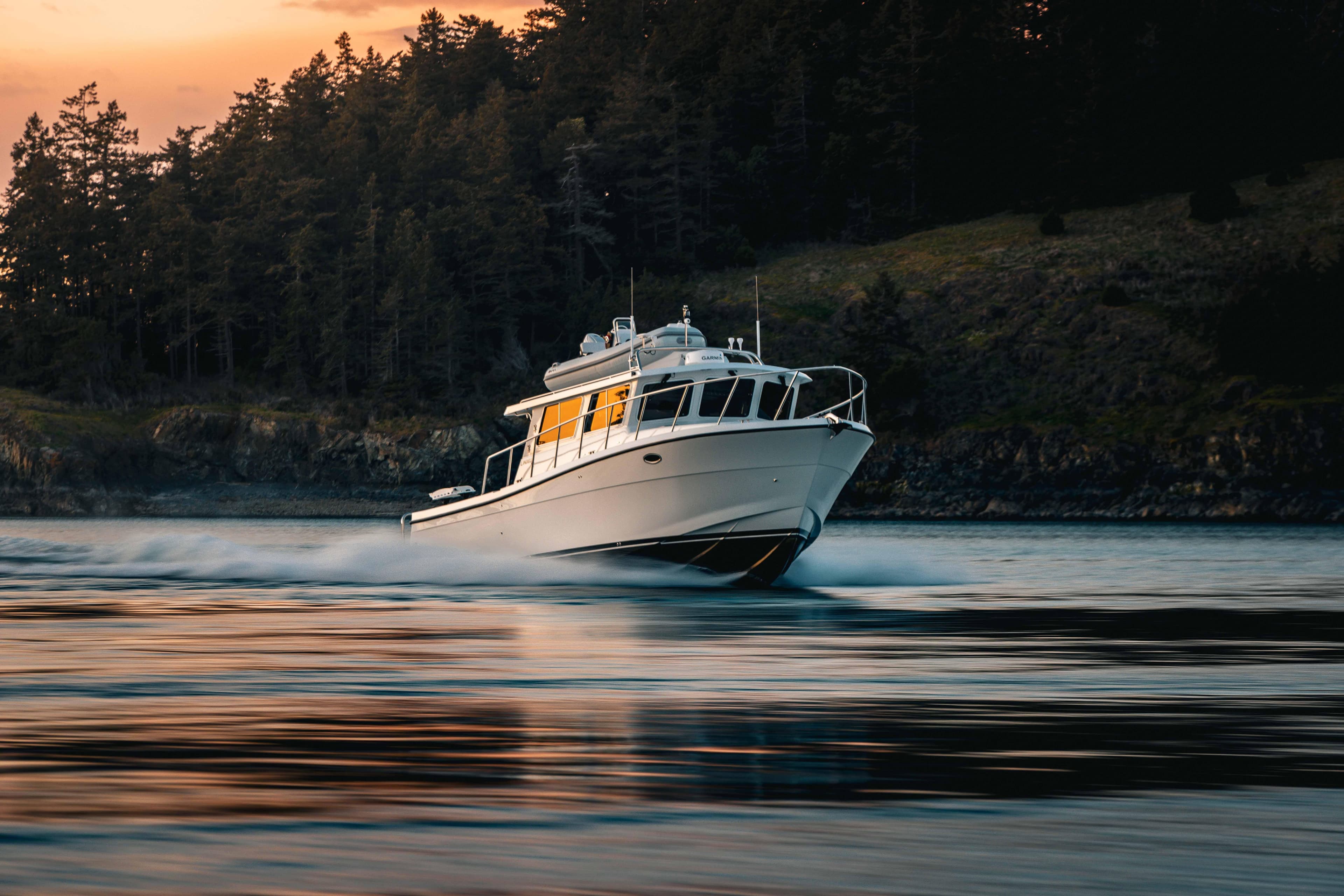 2025 Lindell 42' boat cruising on water at sunset near forested shoreline.