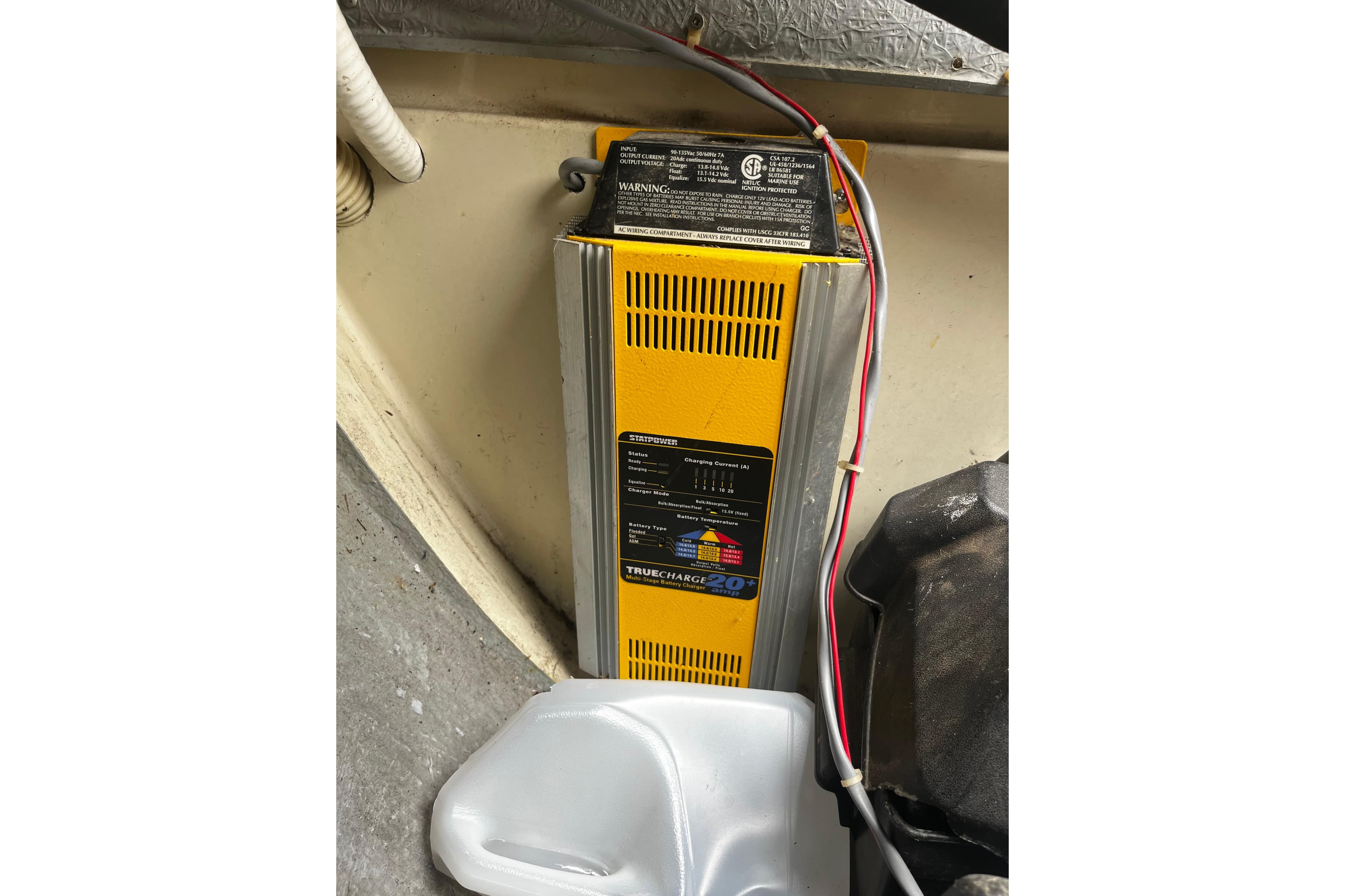 Battery charger installed in a 1988 Mirage 32 boat, with visible wiring and a plastic container.