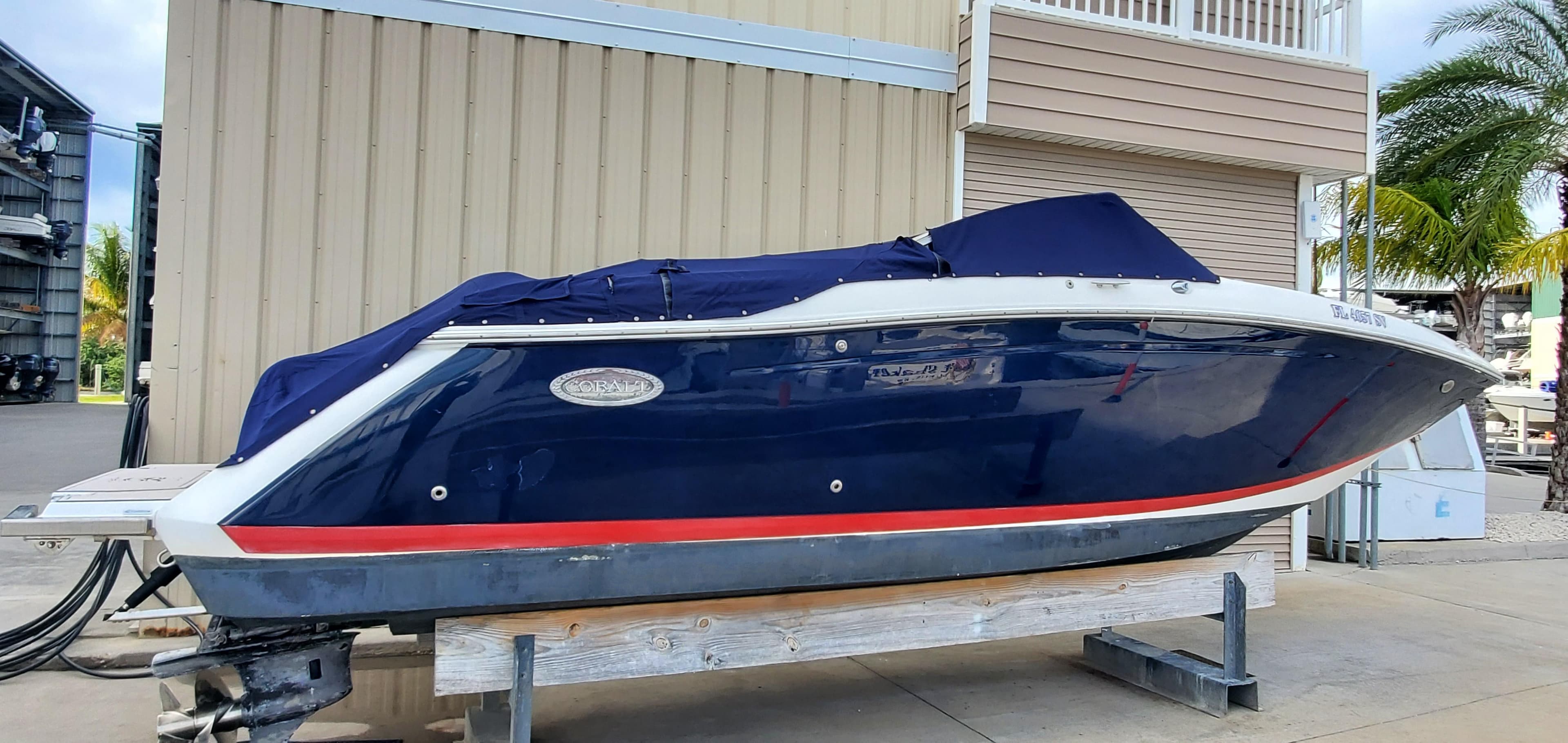 2013 Cobalt 24SD boat with blue cover, docked outdoors near a building and palm tree.