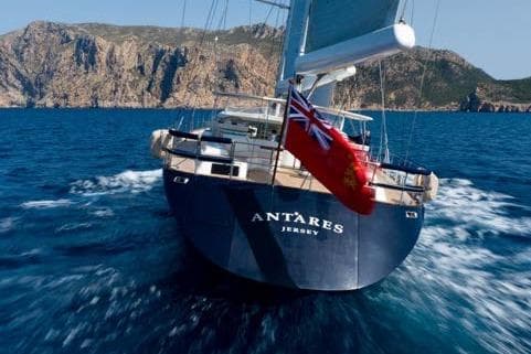 Royal Huisman Antares 2005 yacht sailing near rocky coastline.