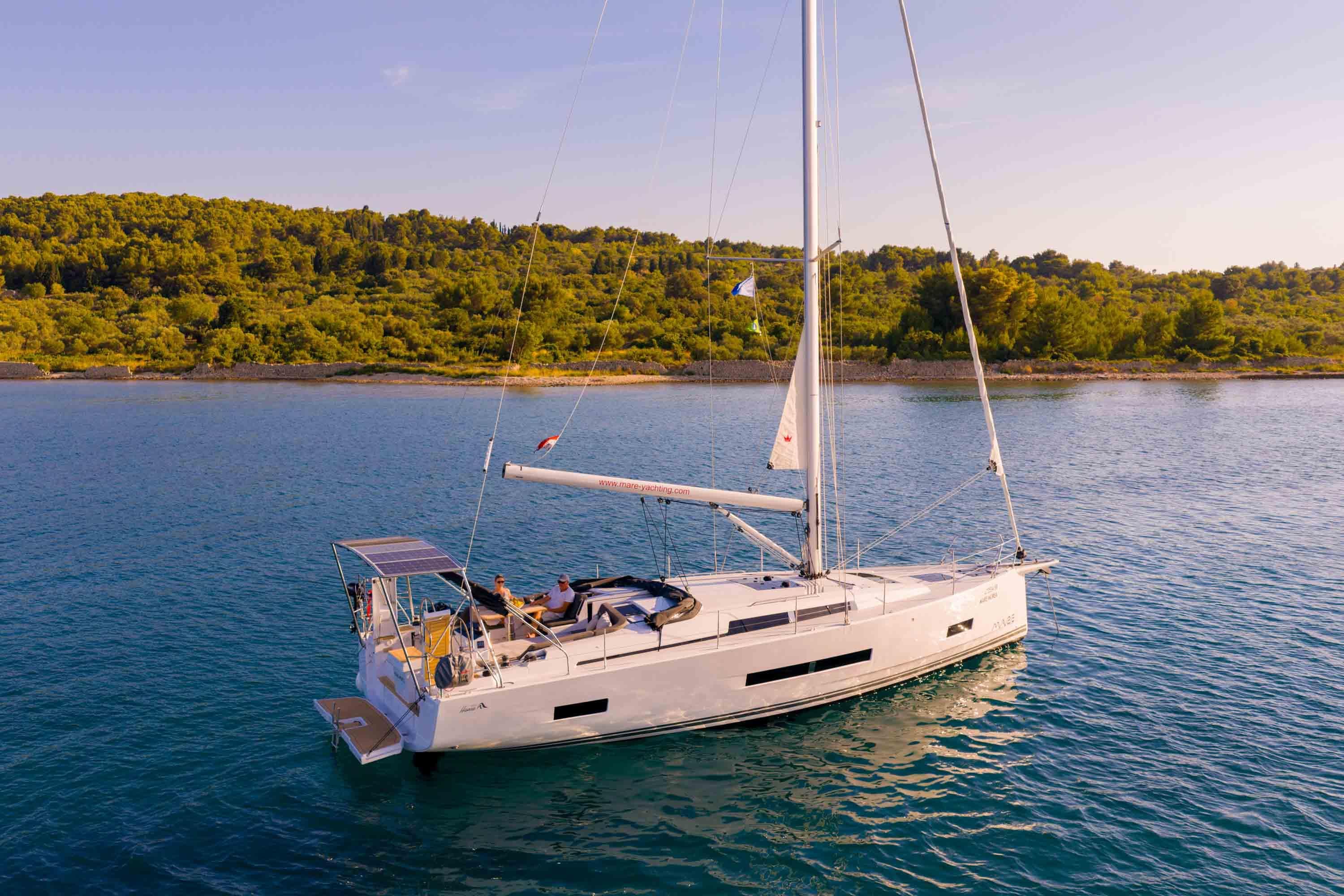 Sailing yacht Hanse 460, 2025 model, cruising on serene waters near a lush coastline.