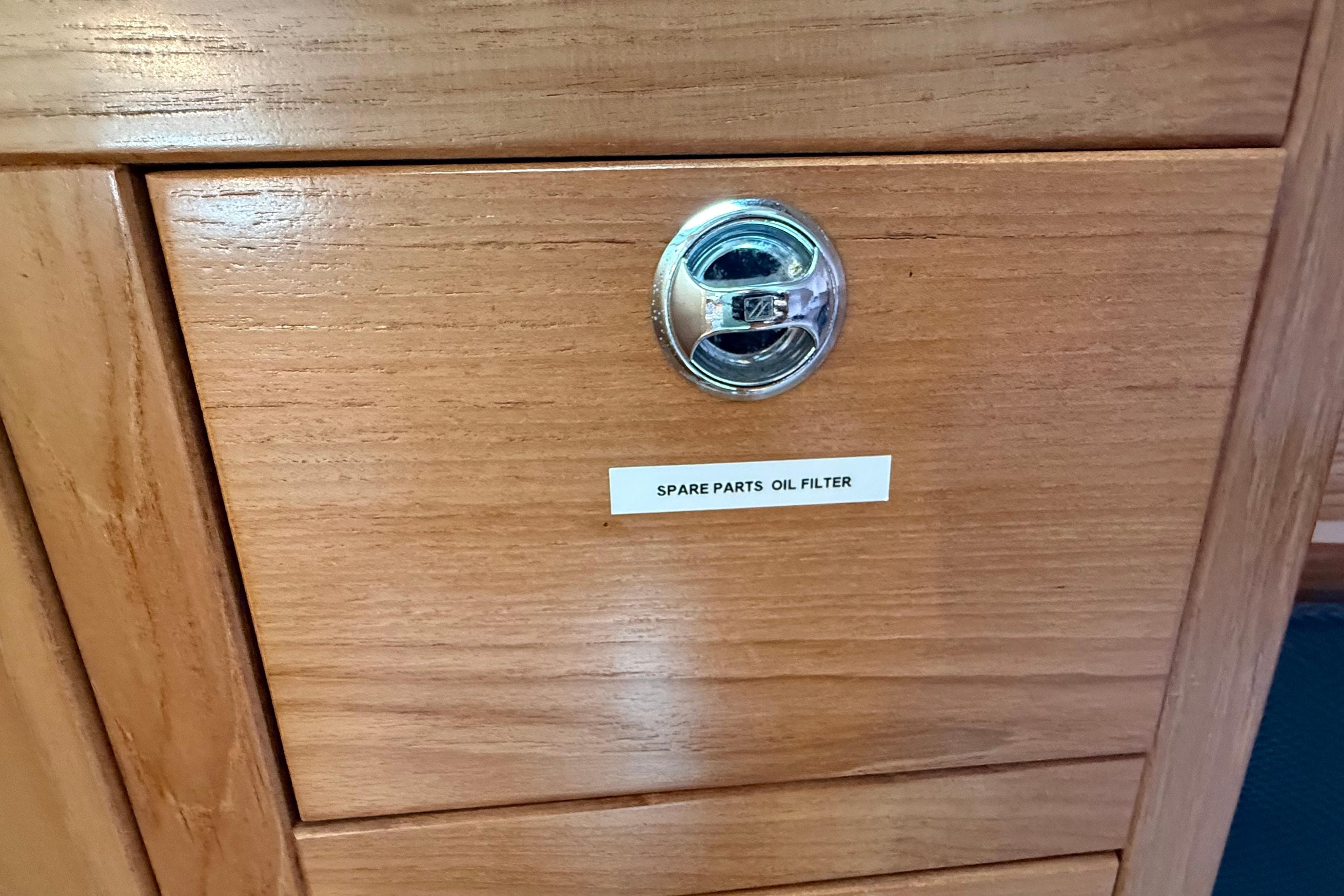Wooden cabinet with metal handle labeled "Spare Parts Oil Filter" on a 2005 Catalina 36 MkII.