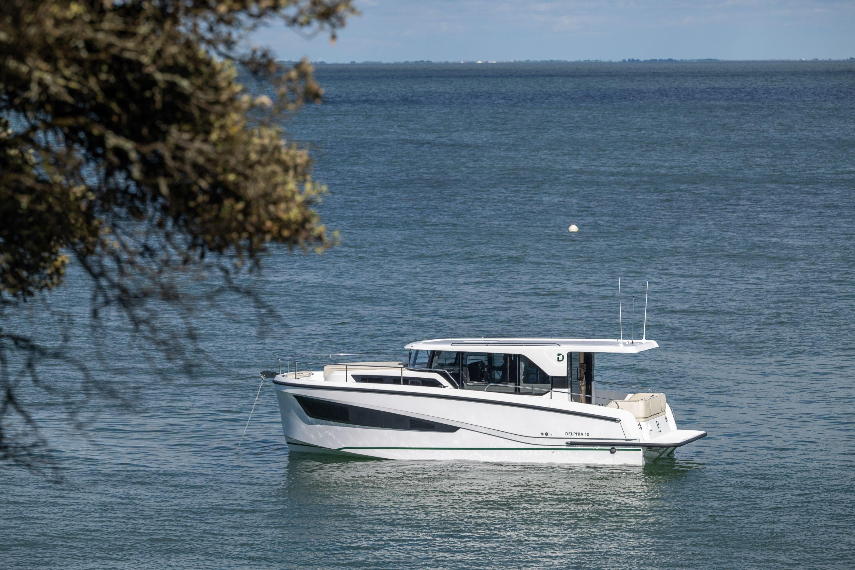 2026 Delphia D10 Sedan boat on calm water, with tree in foreground.