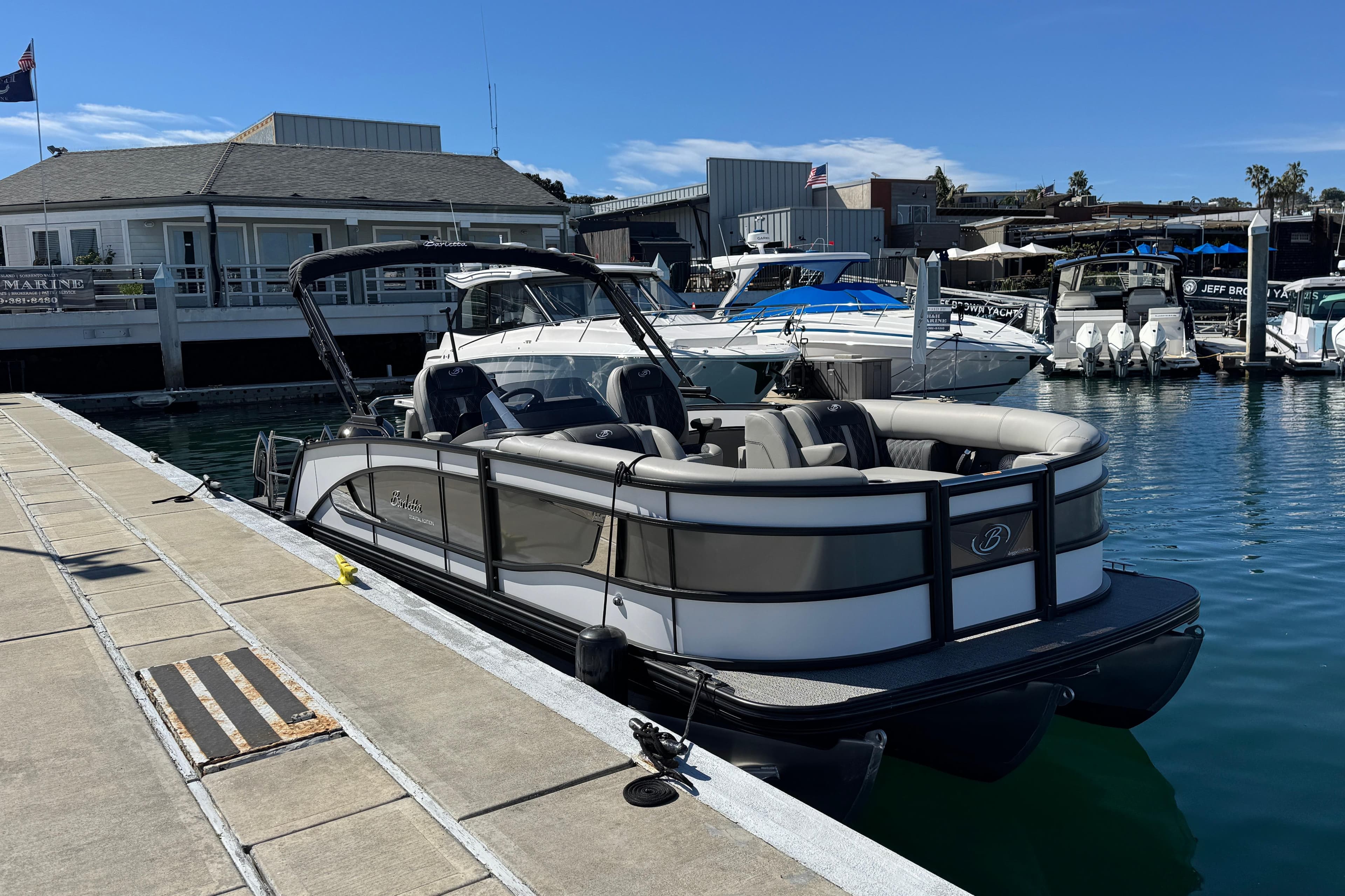2026 Barletta Lusso 23UC pontoon boat docked at a marina under clear blue skies.