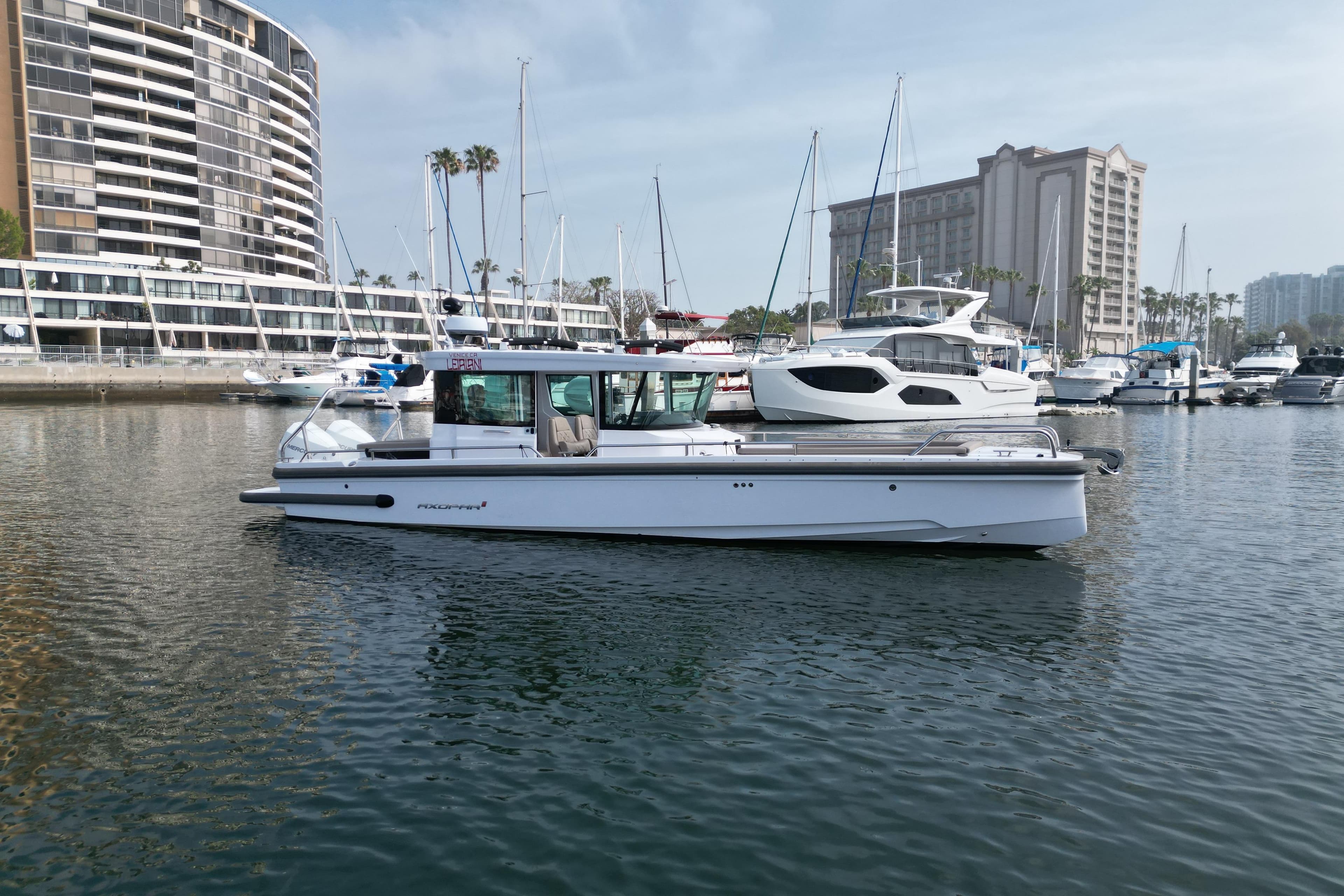 2023 Axopar 28 Cabin boat docked in a marina with modern buildings in the background.