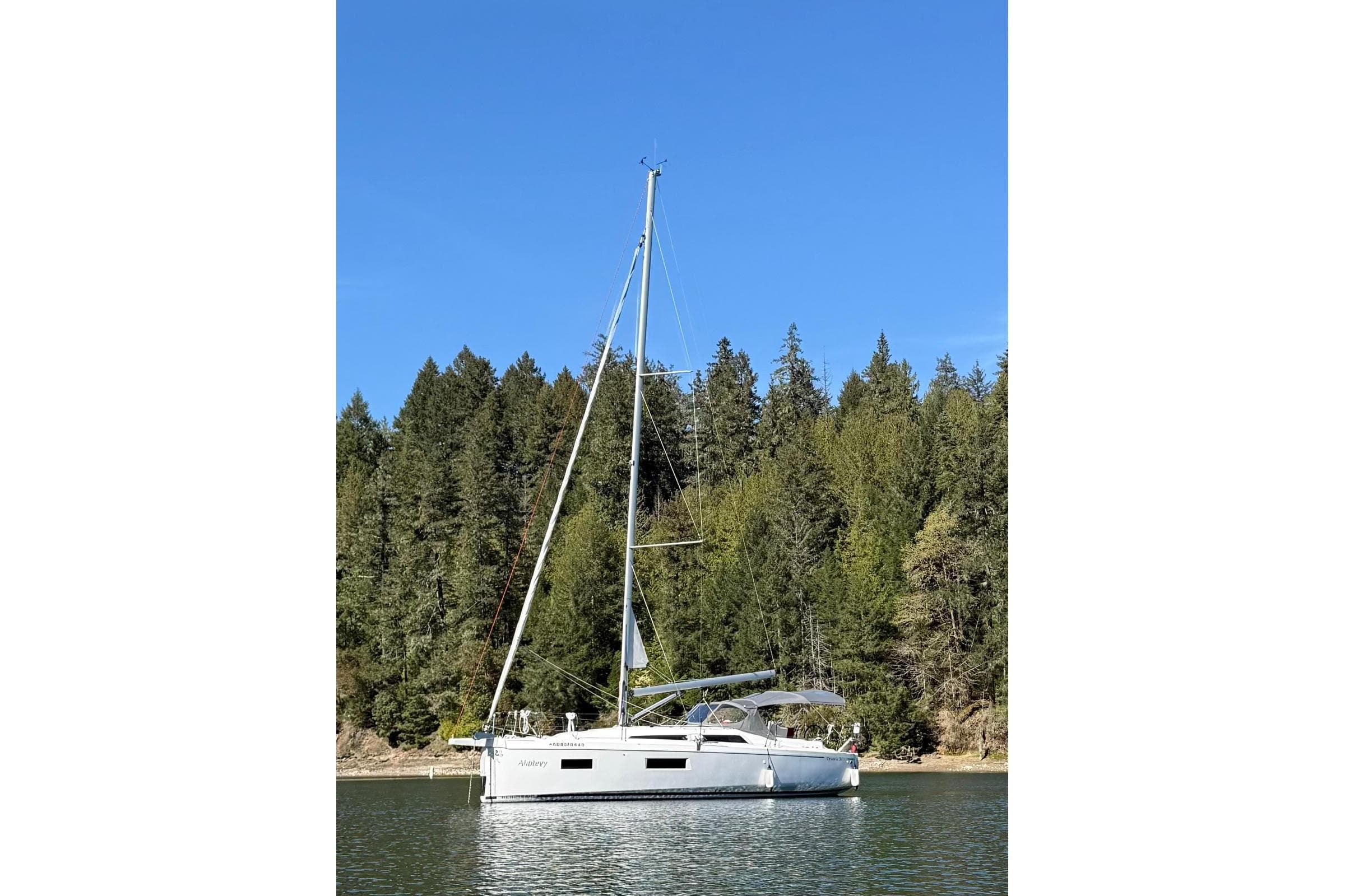 2023 Beneteau Oceanis 34.1 sailboat on calm water, forested background.