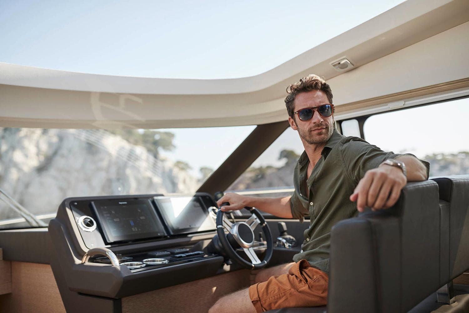 Manufacturer Provided Image: Man steering 2025 Prestige 460 S yacht, wearing sunglasses, in a sunny coastal setting.