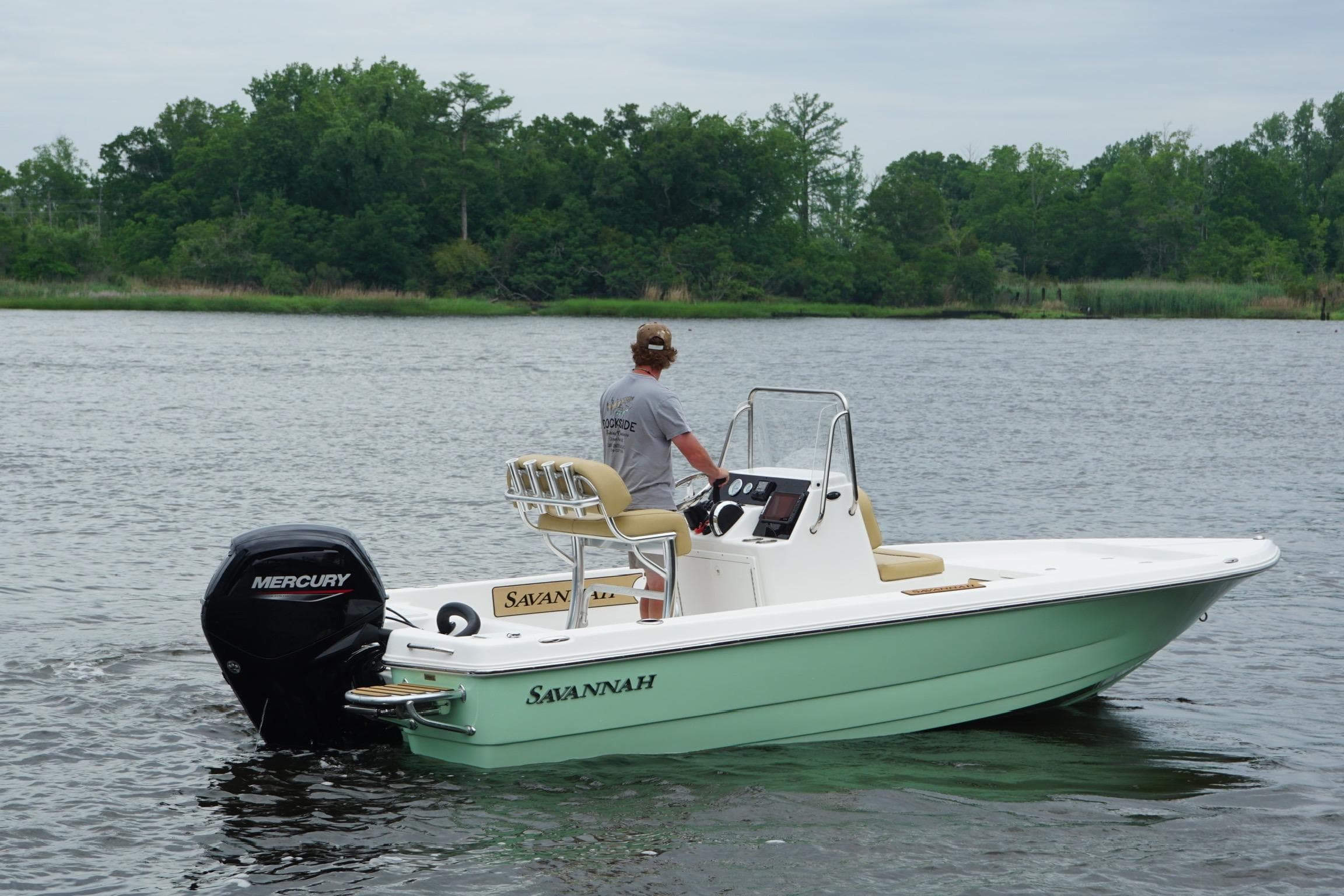 2025 Savannah 190 IS boat on water, featuring Mercury engine, lush green shoreline background.