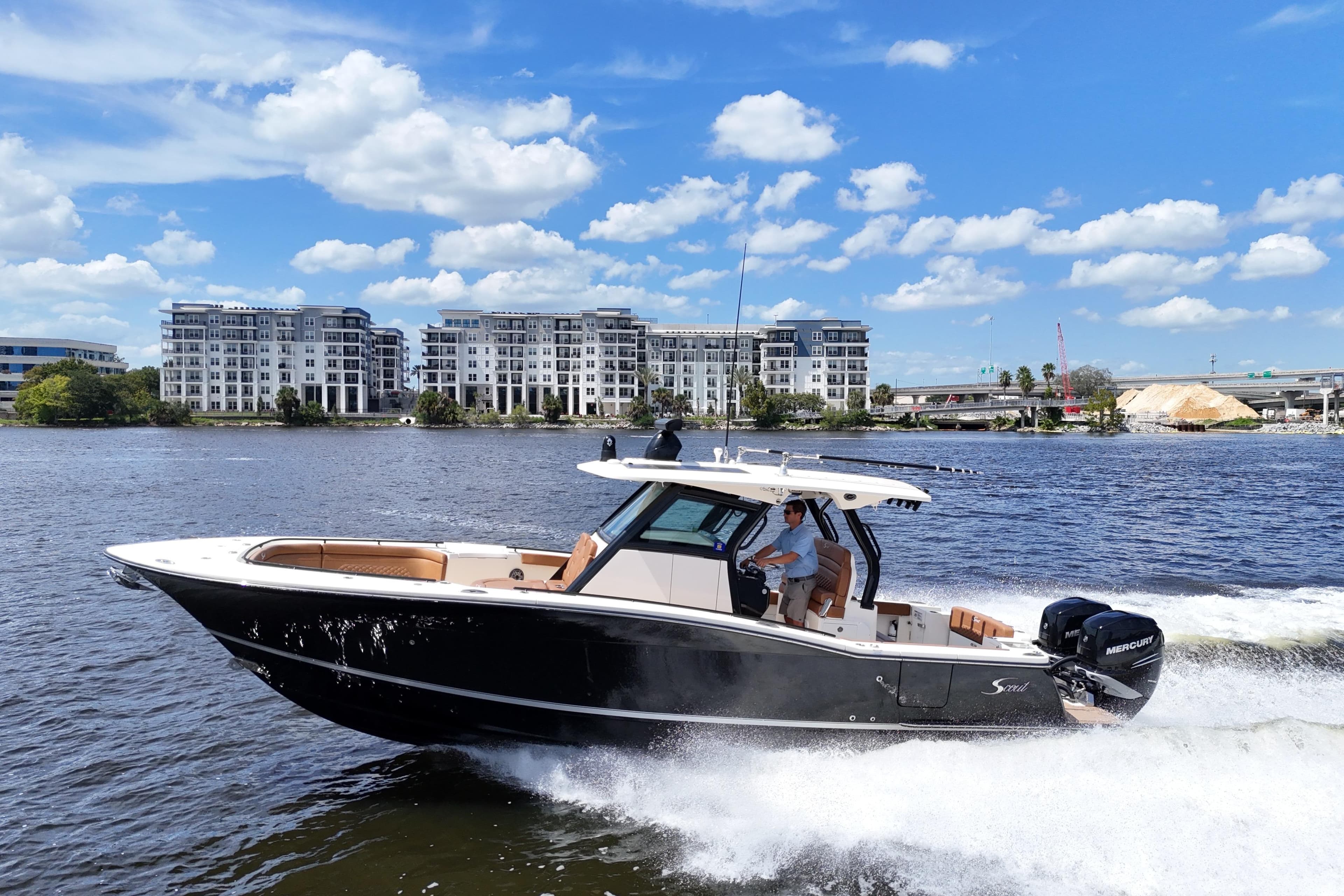 2021 Scout 330 LXF boat cruising on a sunny day near modern waterfront buildings.