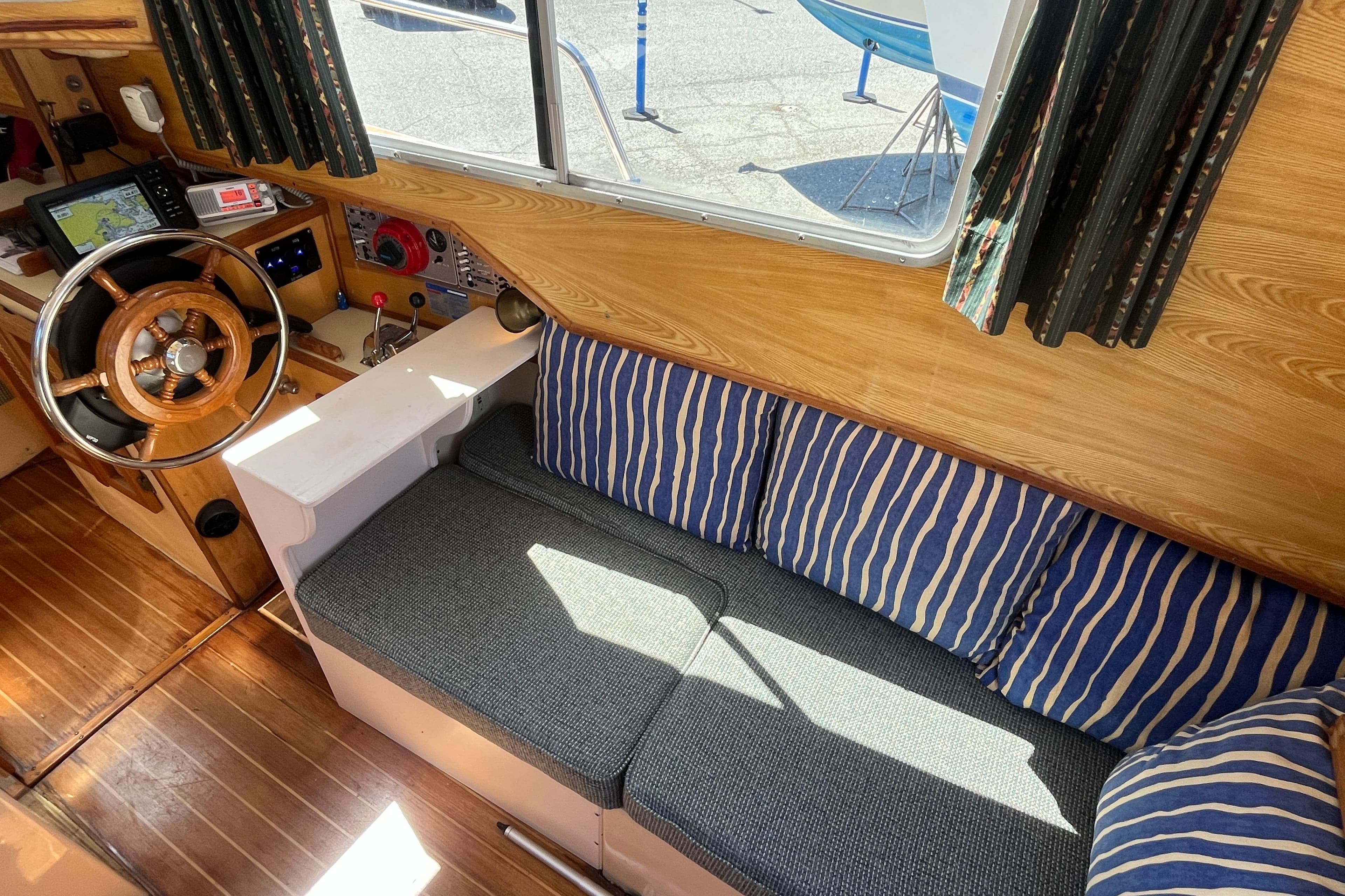 Interior of 1994 Nimble Kodiak Pilothouse Motor Sailor with wooden helm and striped cushions.