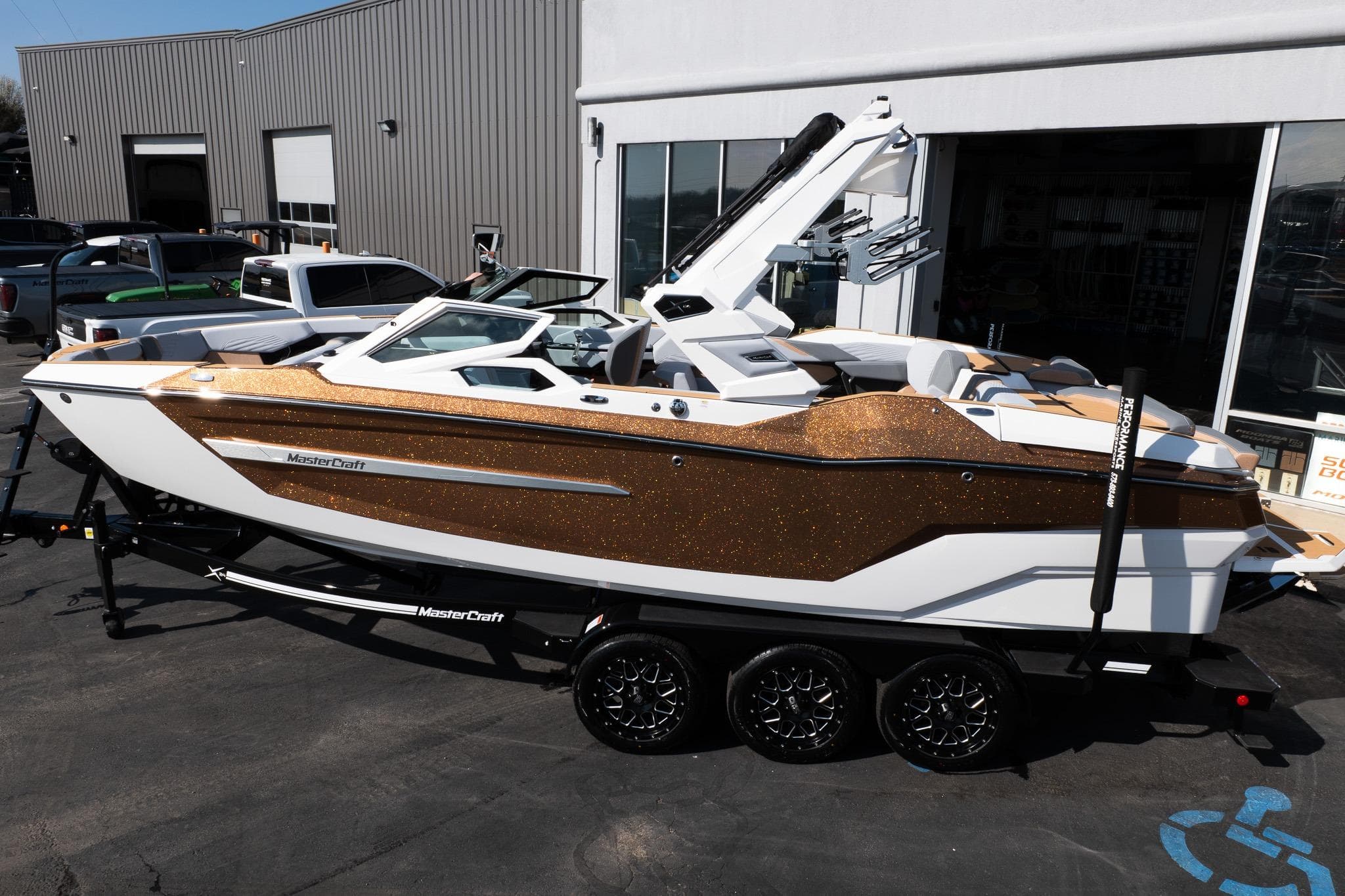2026 MasterCraft X24 boat with gold accents on a trailer, parked outside a building.