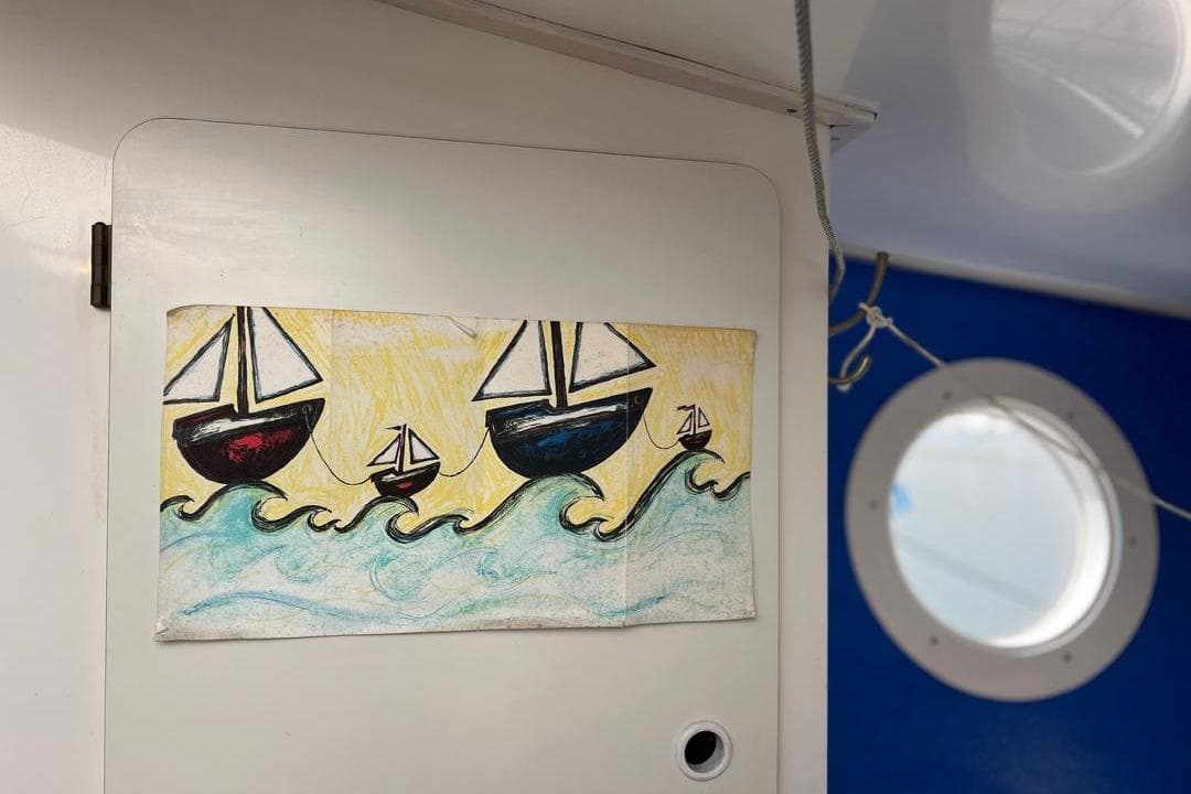 Colorful sailboat drawing on a wall inside a boat with a porthole window.