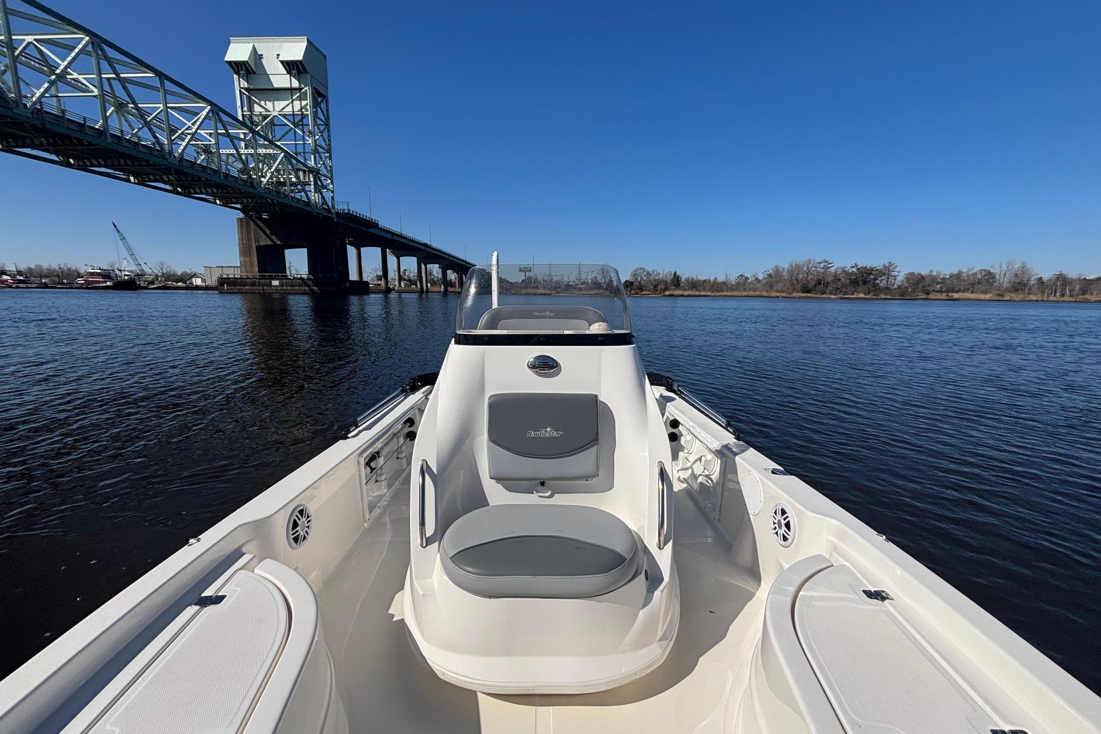 2023 NauticStar 215 XTS boat on water near a bridge under clear blue sky.