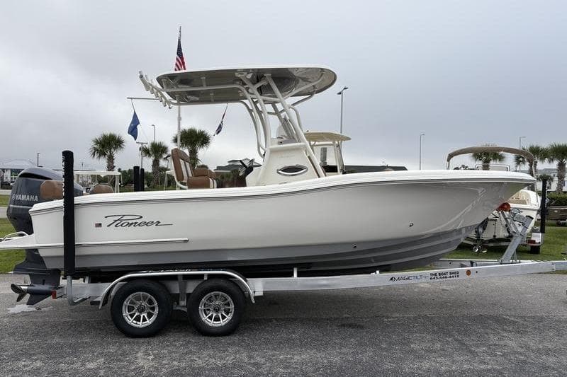 2026 Pioneer 222 Sportfish boat on trailer, side view, with flags in background.