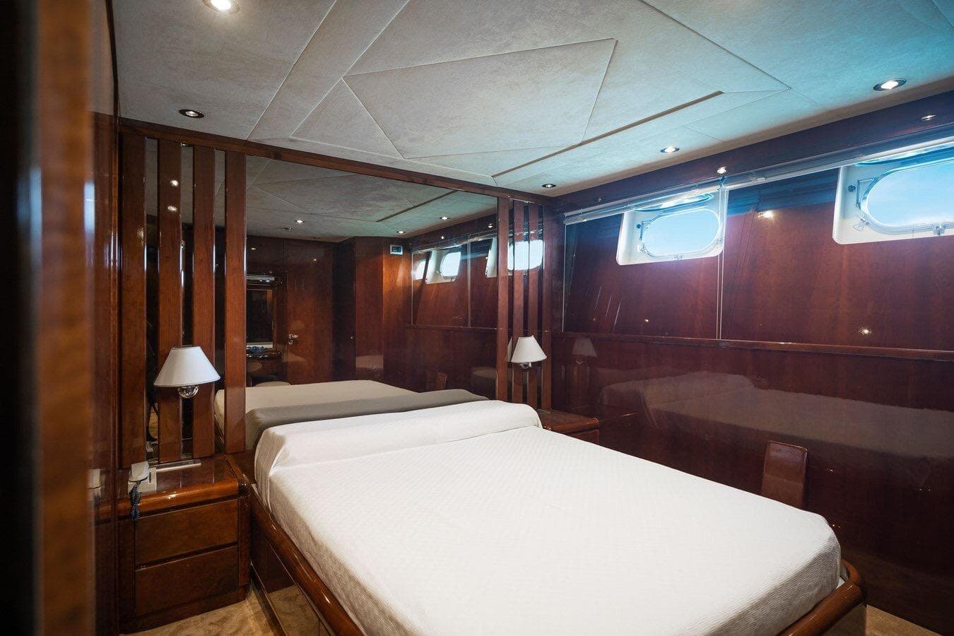 Luxurious bedroom interior on 1996 Falcon 92 yacht with wood paneling and porthole windows.