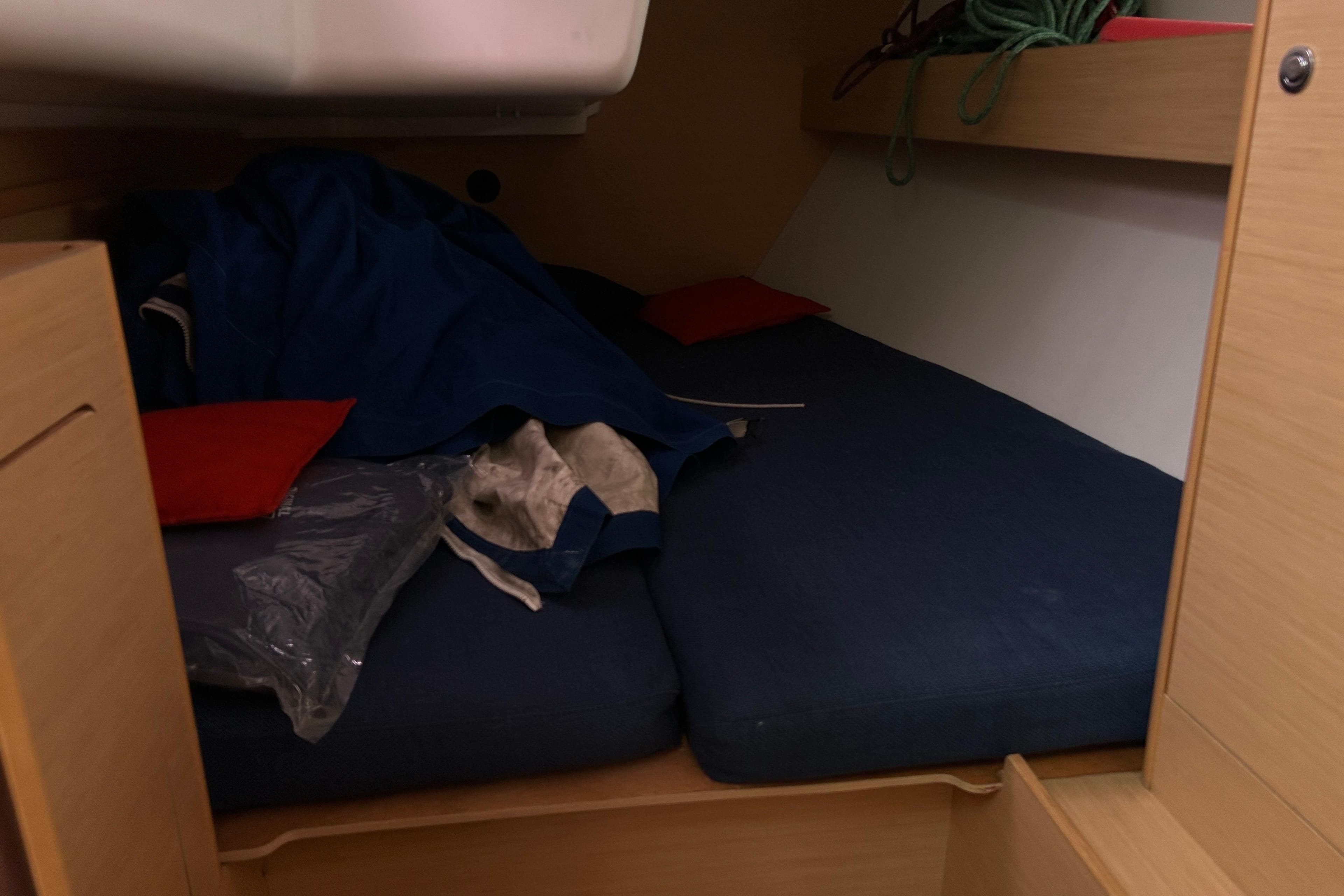 Cozy cabin interior of 2012 Beneteau First 40 sailboat with blue bedding and red pillows.