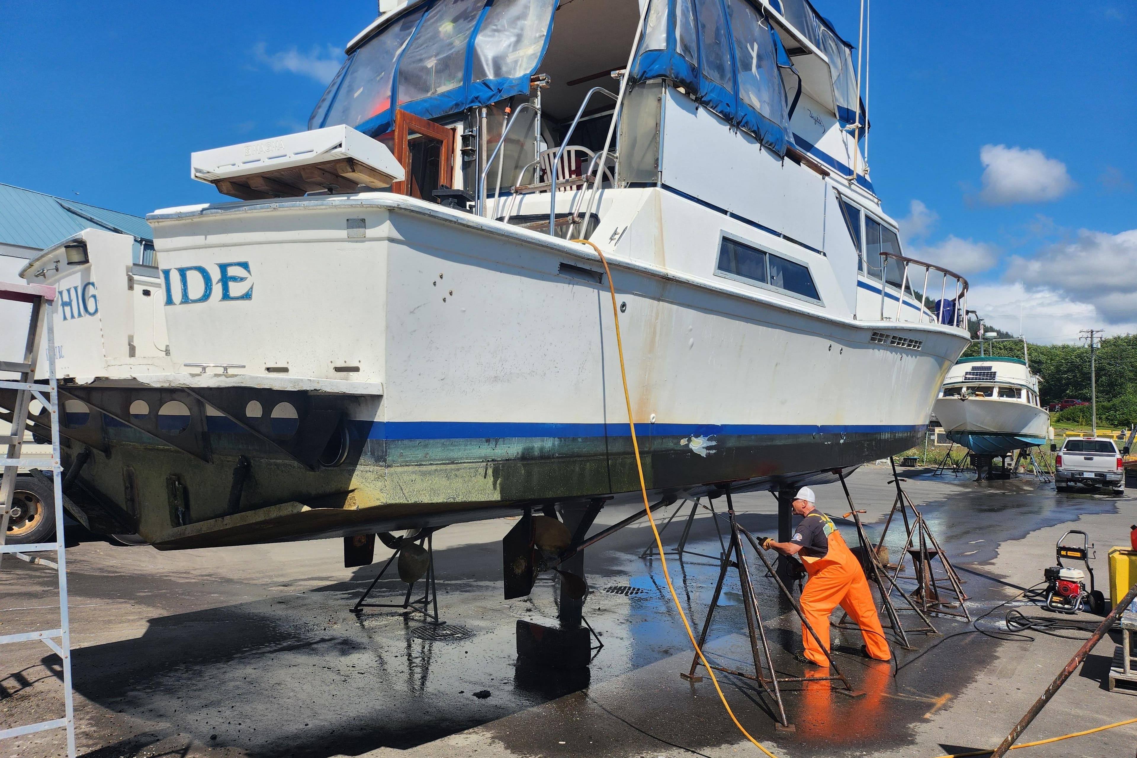 1981 Uniflite MY boat undergoing maintenance at a shipyard, worker cleaning hull.
