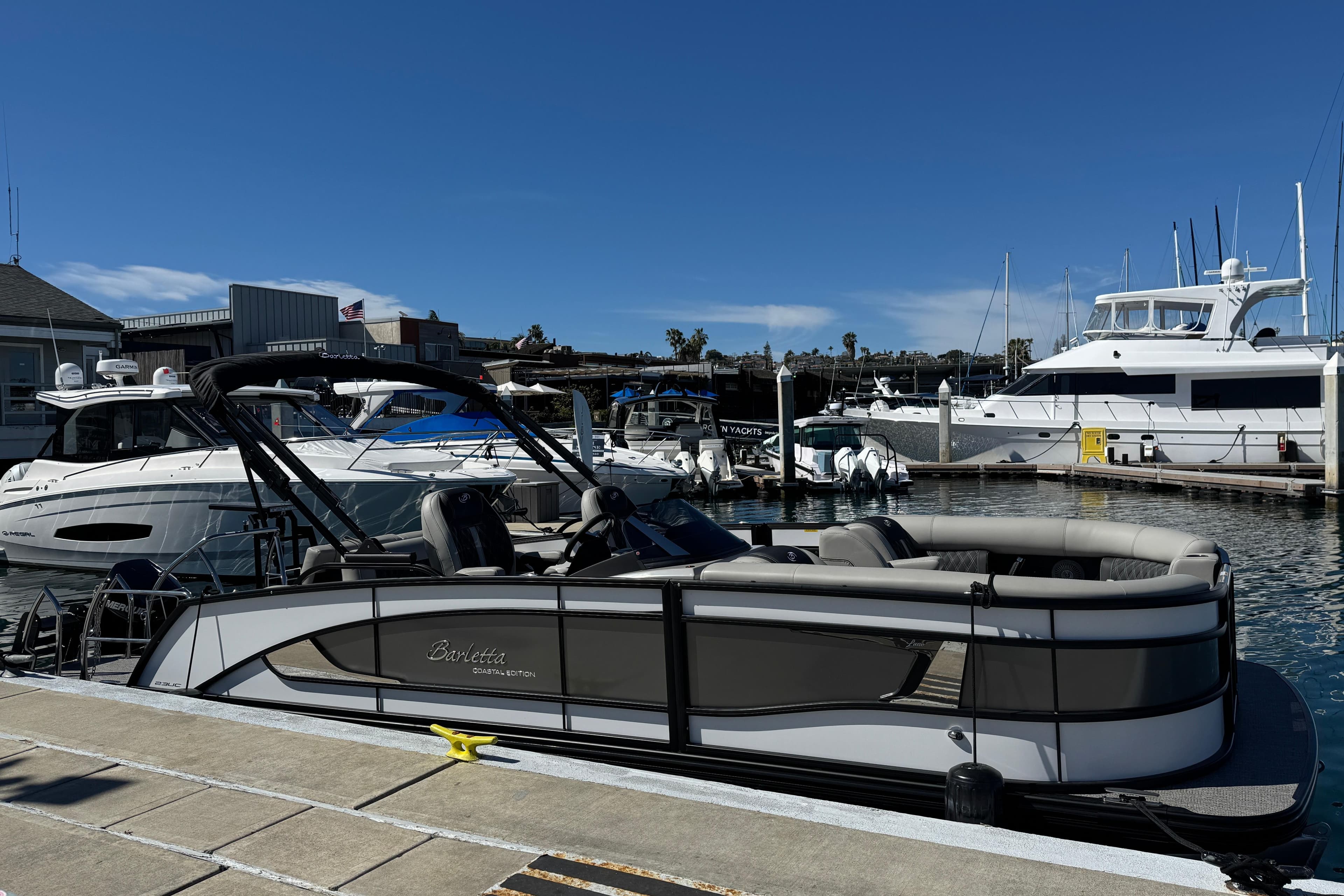 2026 Barletta Lusso 23UC pontoon boat docked in a marina under clear blue skies.