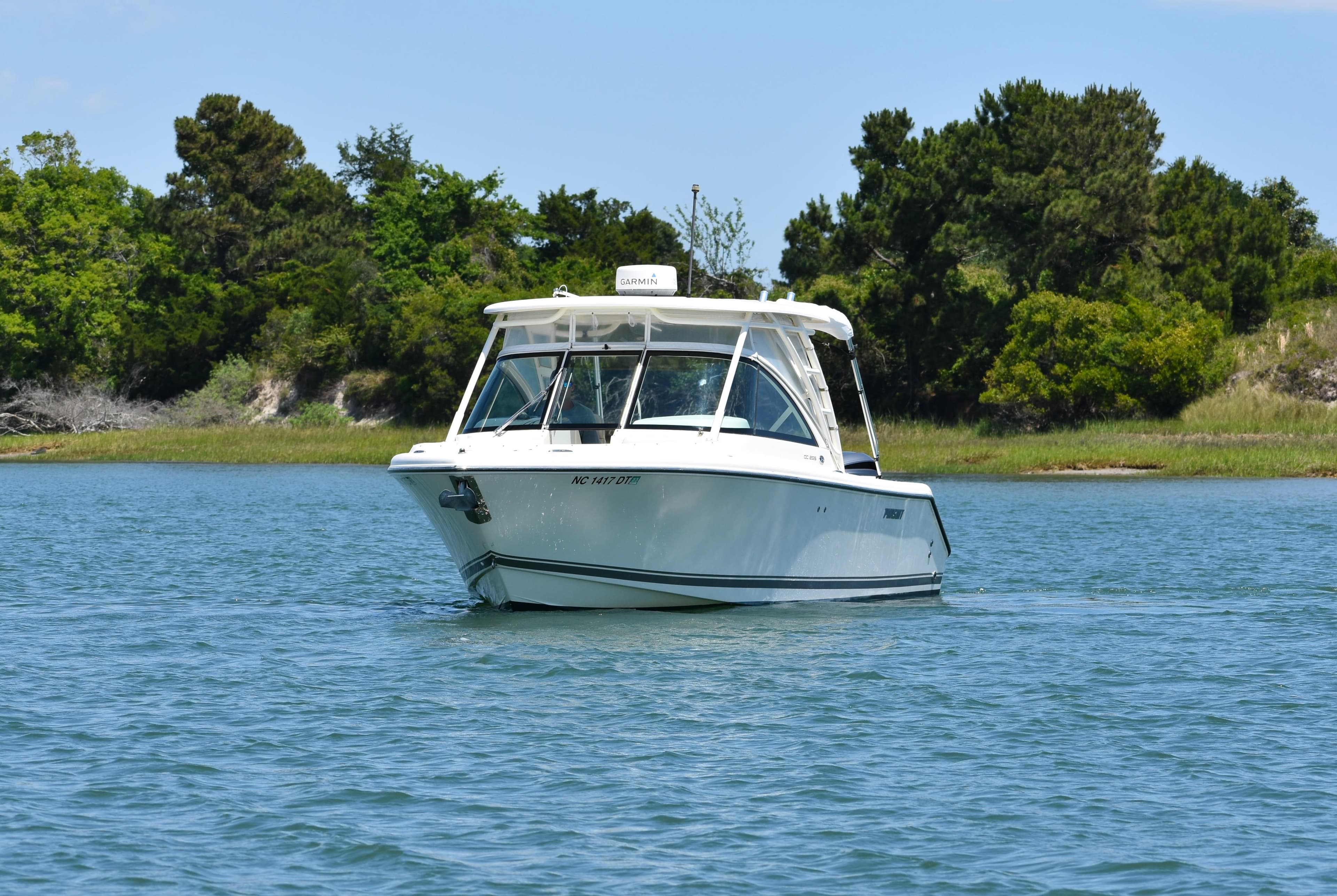 2012 Pursuit DC 265 Dual Console boat on calm water, surrounded by lush greenery.