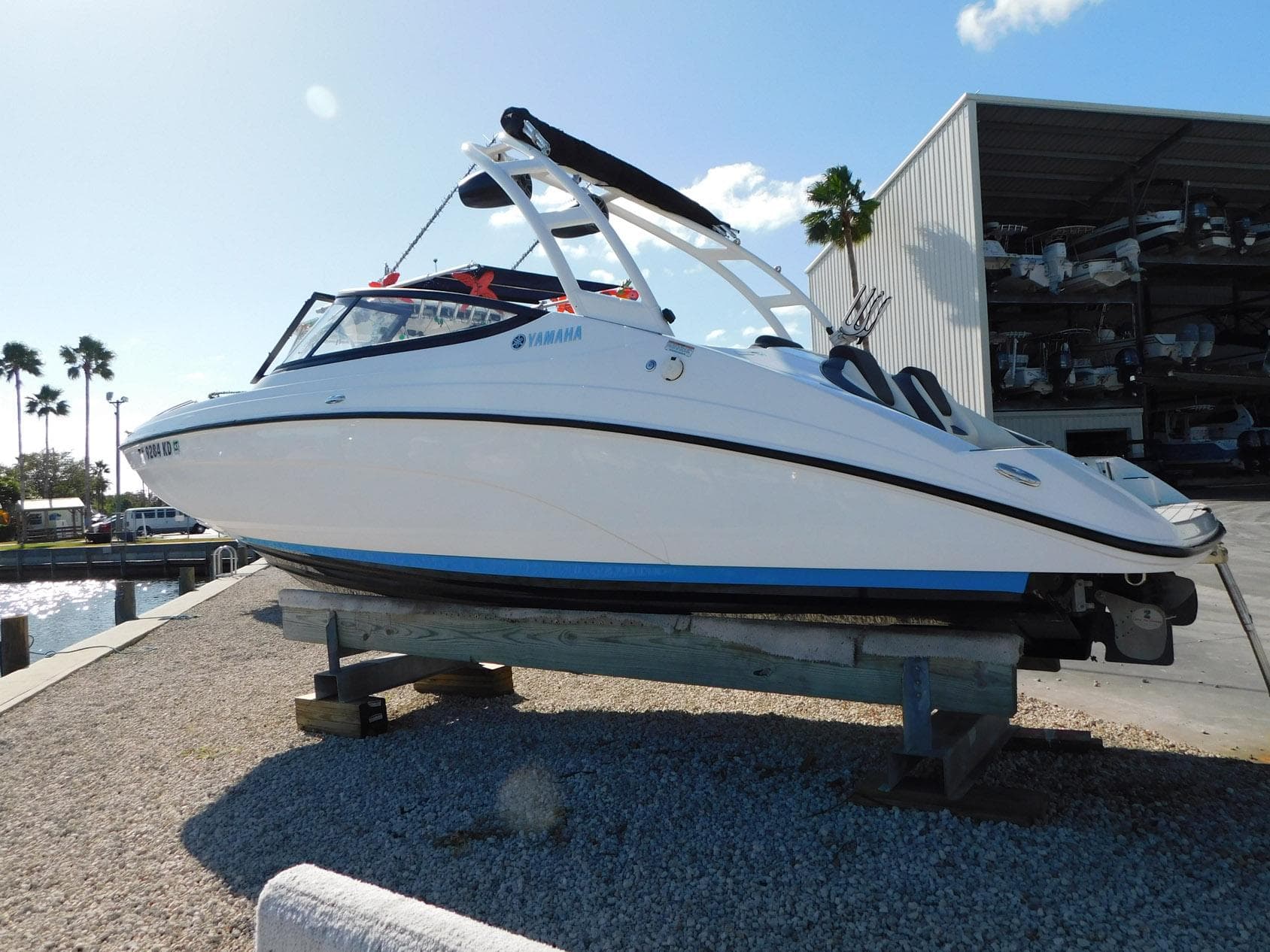 2021 Yamaha AR210 boat on display, white hull, dockside with palm trees and storage building.