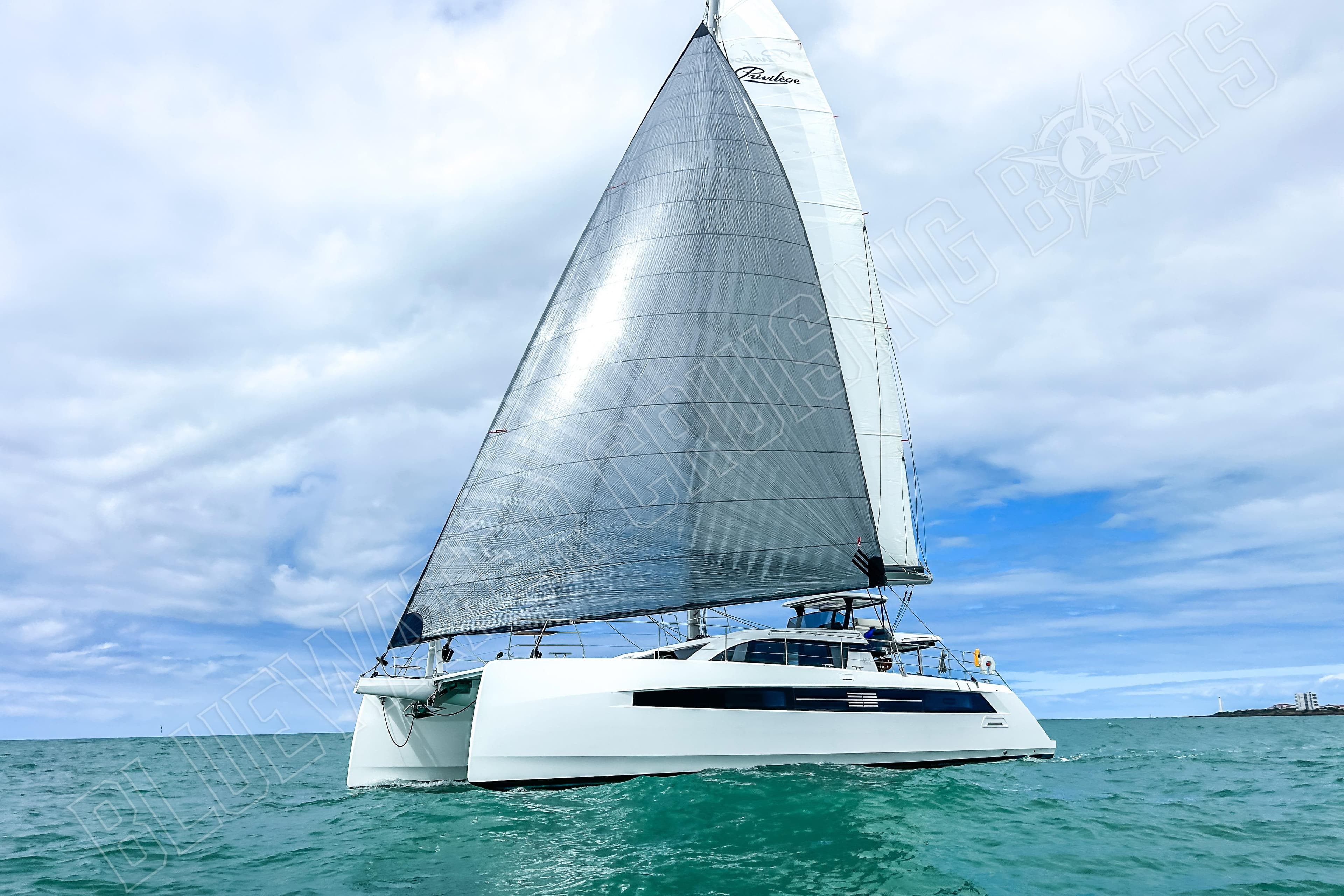 Sailing catamaran Privilege 580, 2025 model, cruising on open sea under cloudy skies.