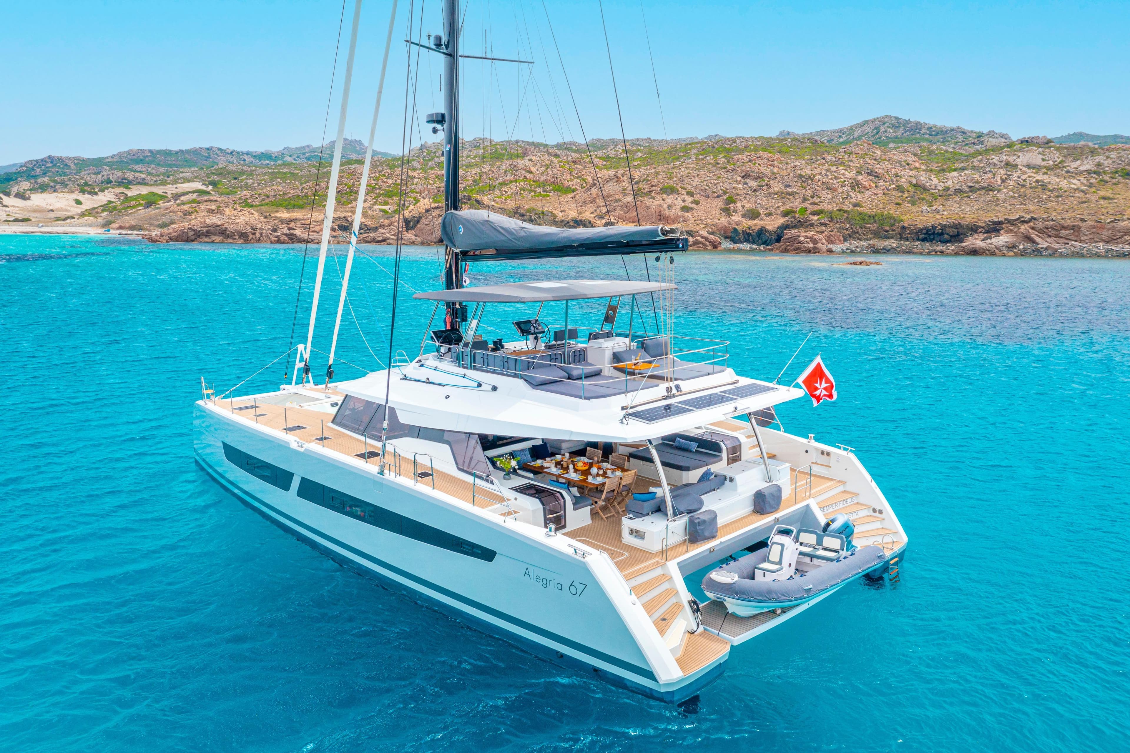 2022 Fountaine Pajot Alegria 67 Catamaran sailing in clear turquoise waters near rocky coastline.