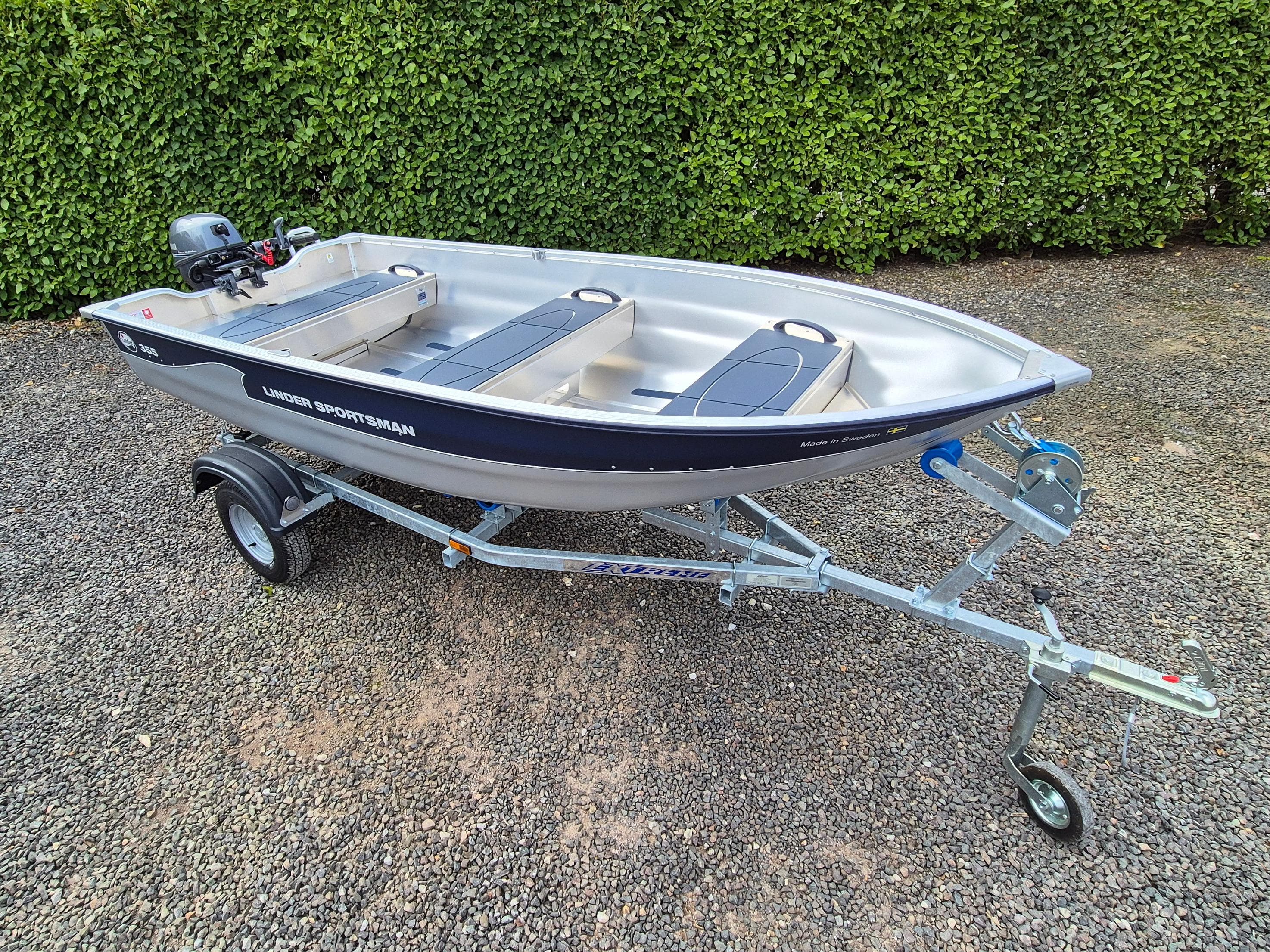 2023 Linder Sportsman 355 boat on trailer, parked on gravel with green hedge background.