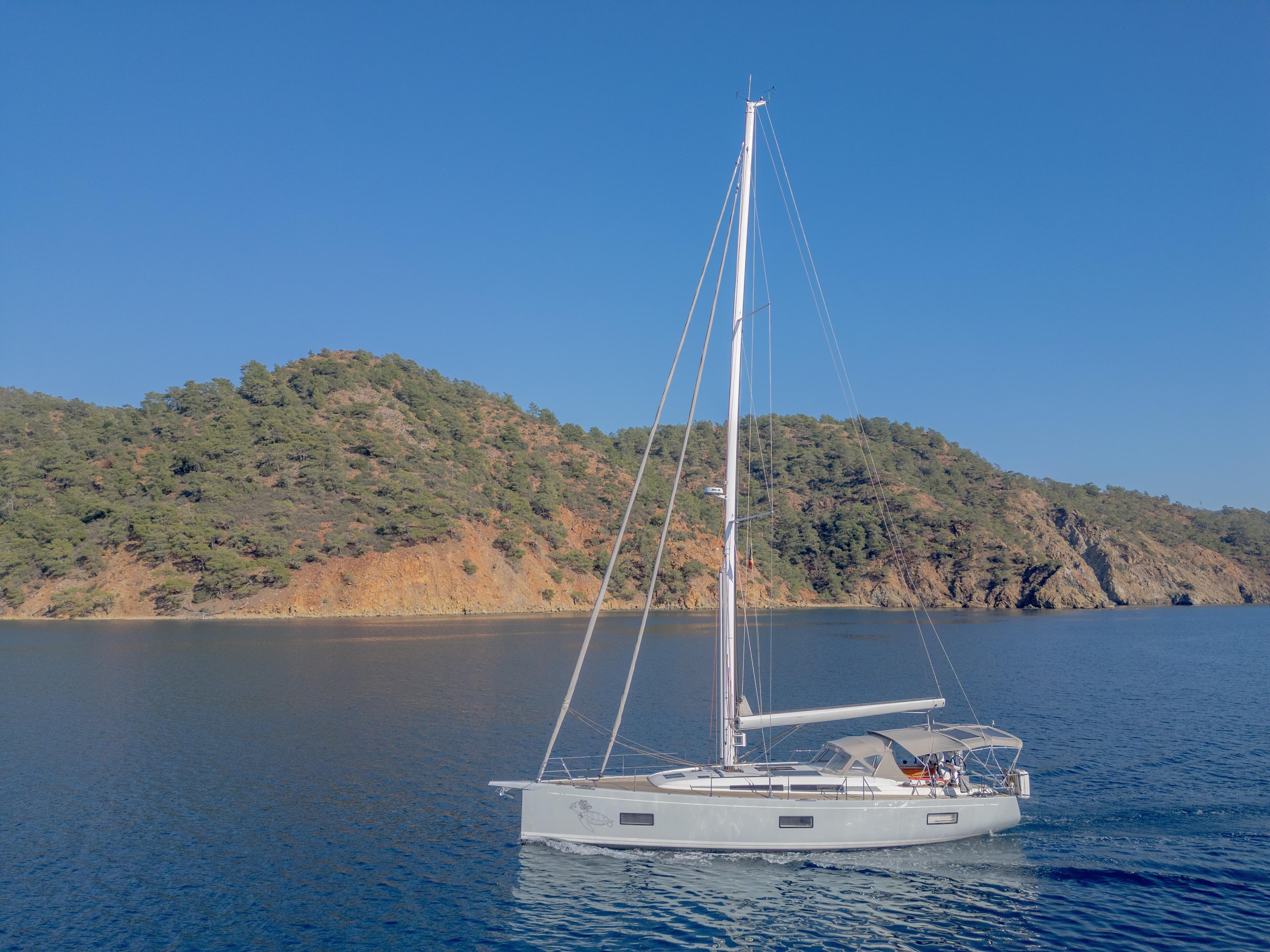 Sailing yacht Nautor Swan 48 (2020) on calm sea near a forested coastline.