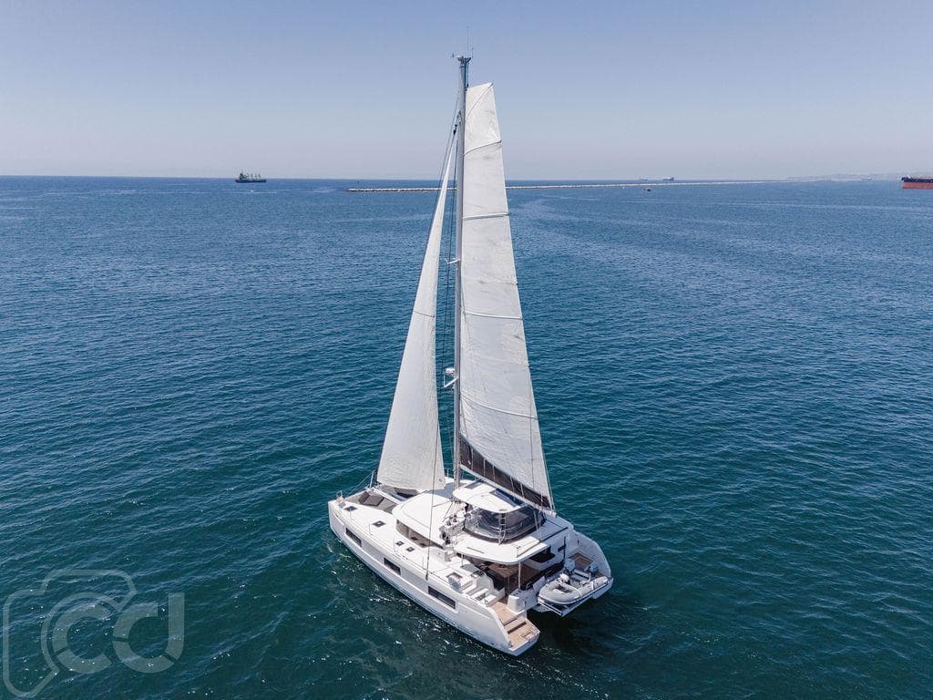 2021 Lagoon 46 catamaran sailing on open sea under clear blue sky.