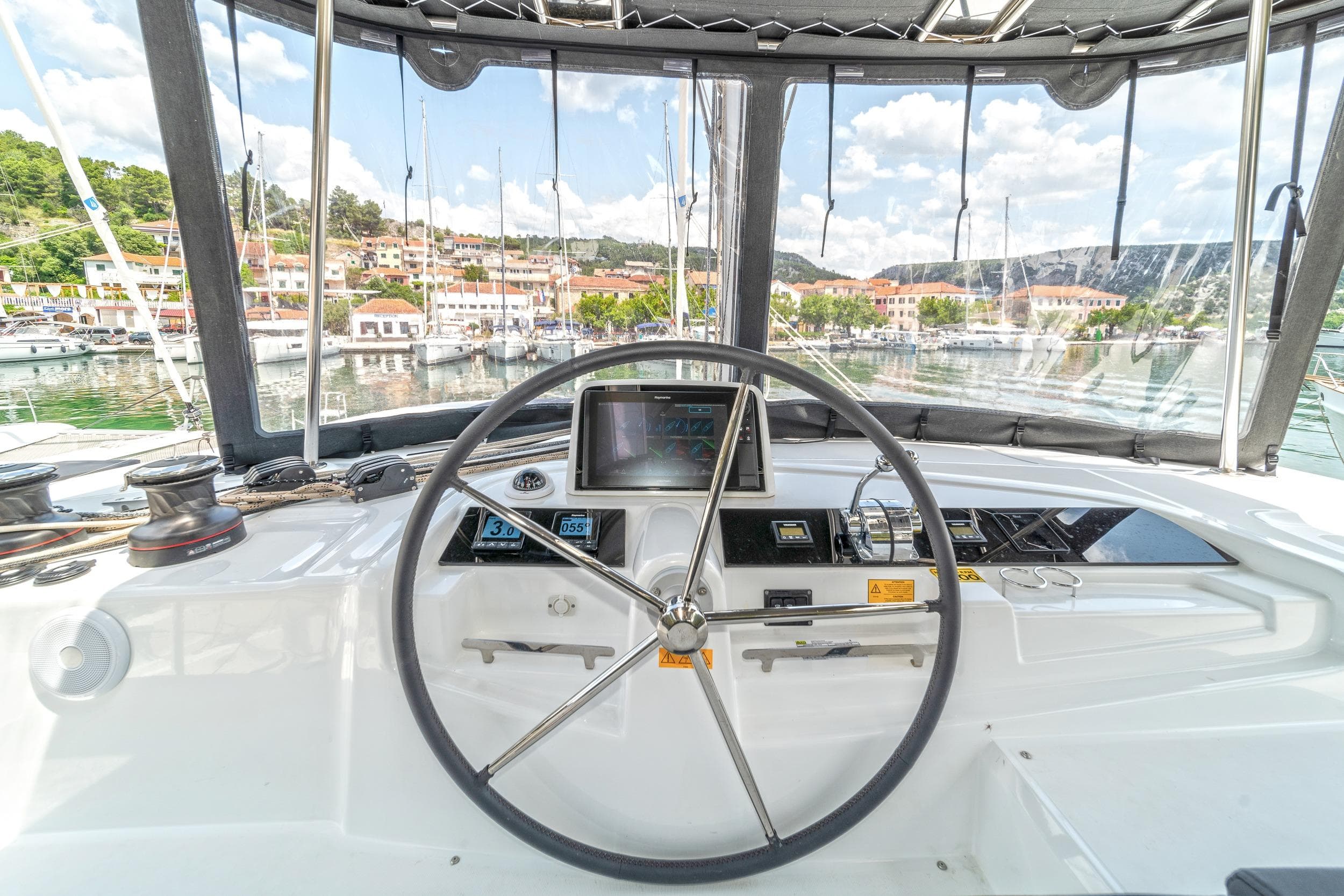 Cockpit view of 2023 Lagoon 46 catamaran, featuring steering wheel and navigation controls.