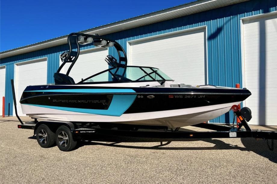2014 Nautique Super Air Nautique 210 boat on trailer, parked outside blue building.