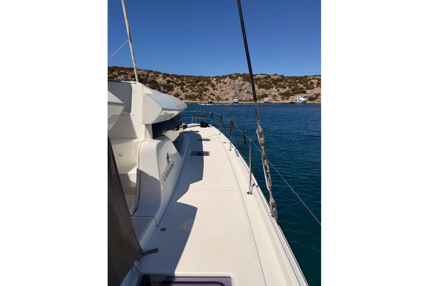 2020 Lagoon 46 catamaran sailing in clear blue waters near rocky coastline.